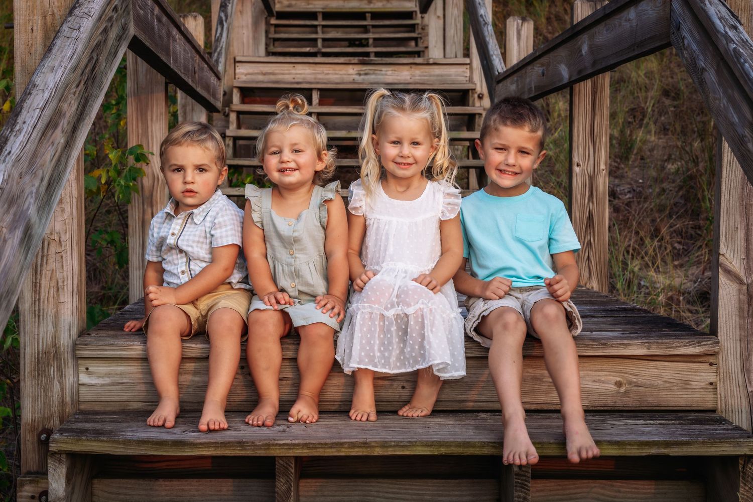 Four young children sitting together on wooden steps outdoors.