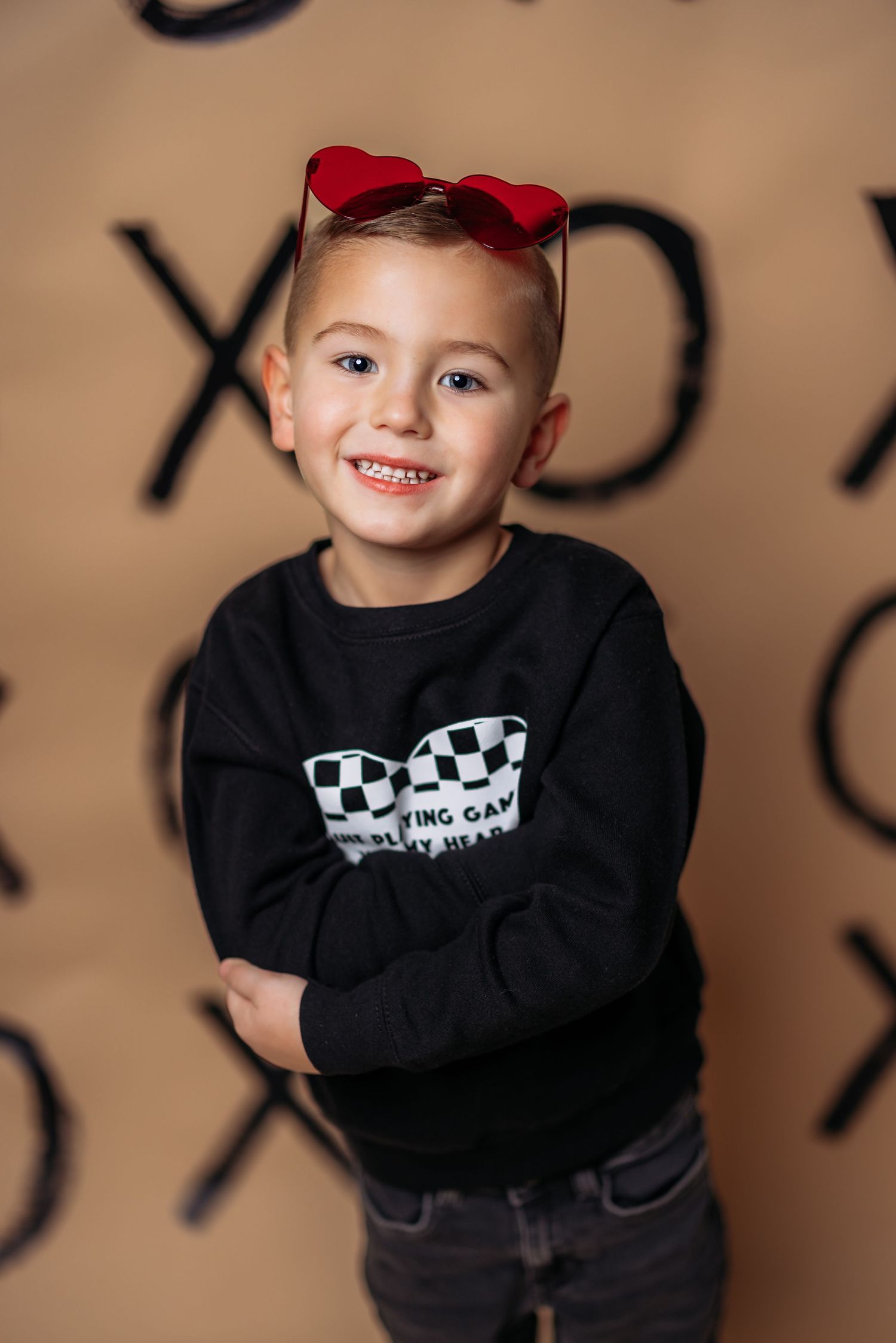 Child in black racing sweatshirt poses against background with red sunglasses.