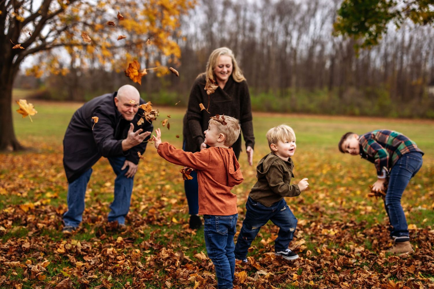 Family playing together in fallen autumn leaves during a fun outdoor photoshoot.