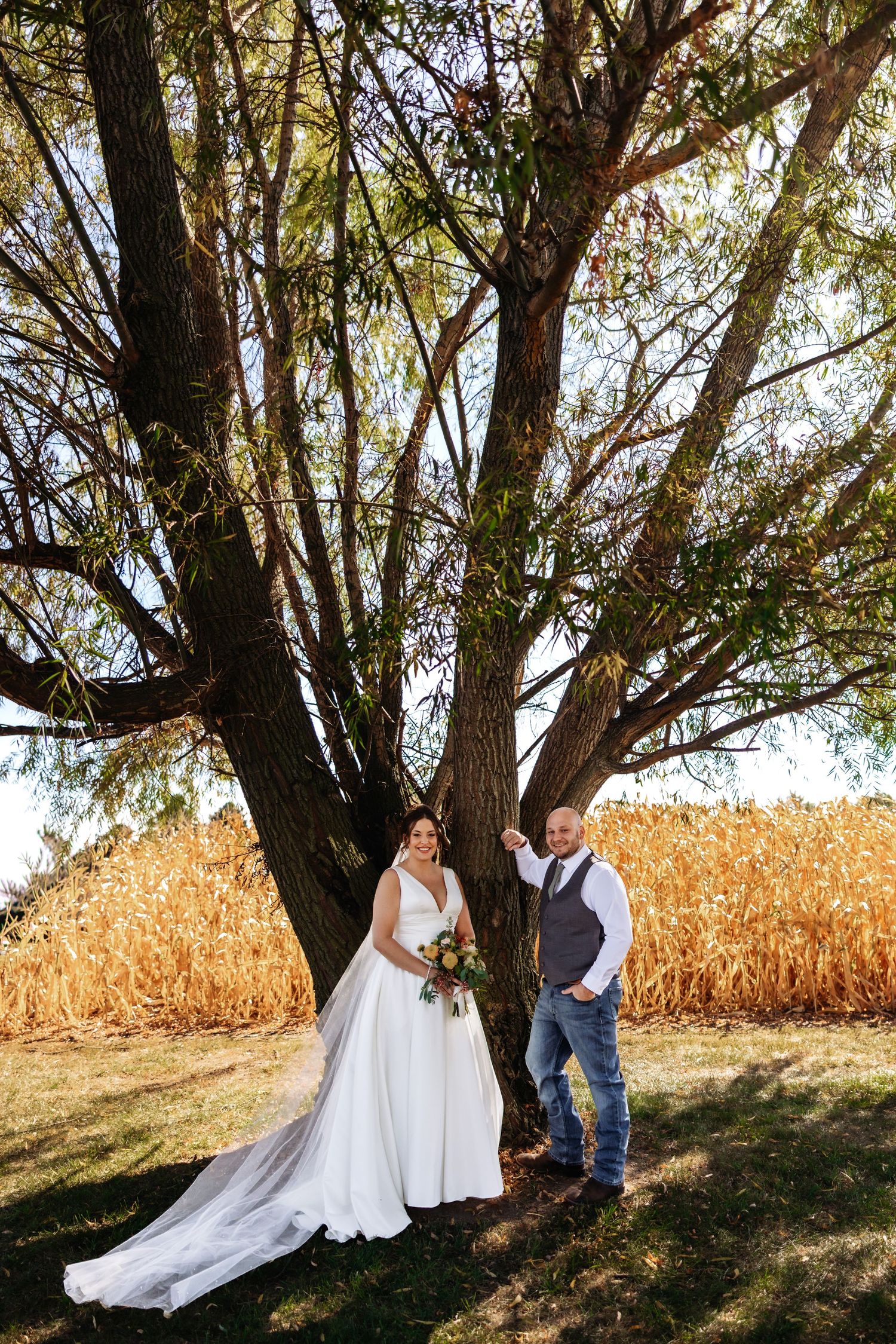 A couple shares romantic moments in a rustic outdoor setting with cornfields and trees during their wedding photoshoot.