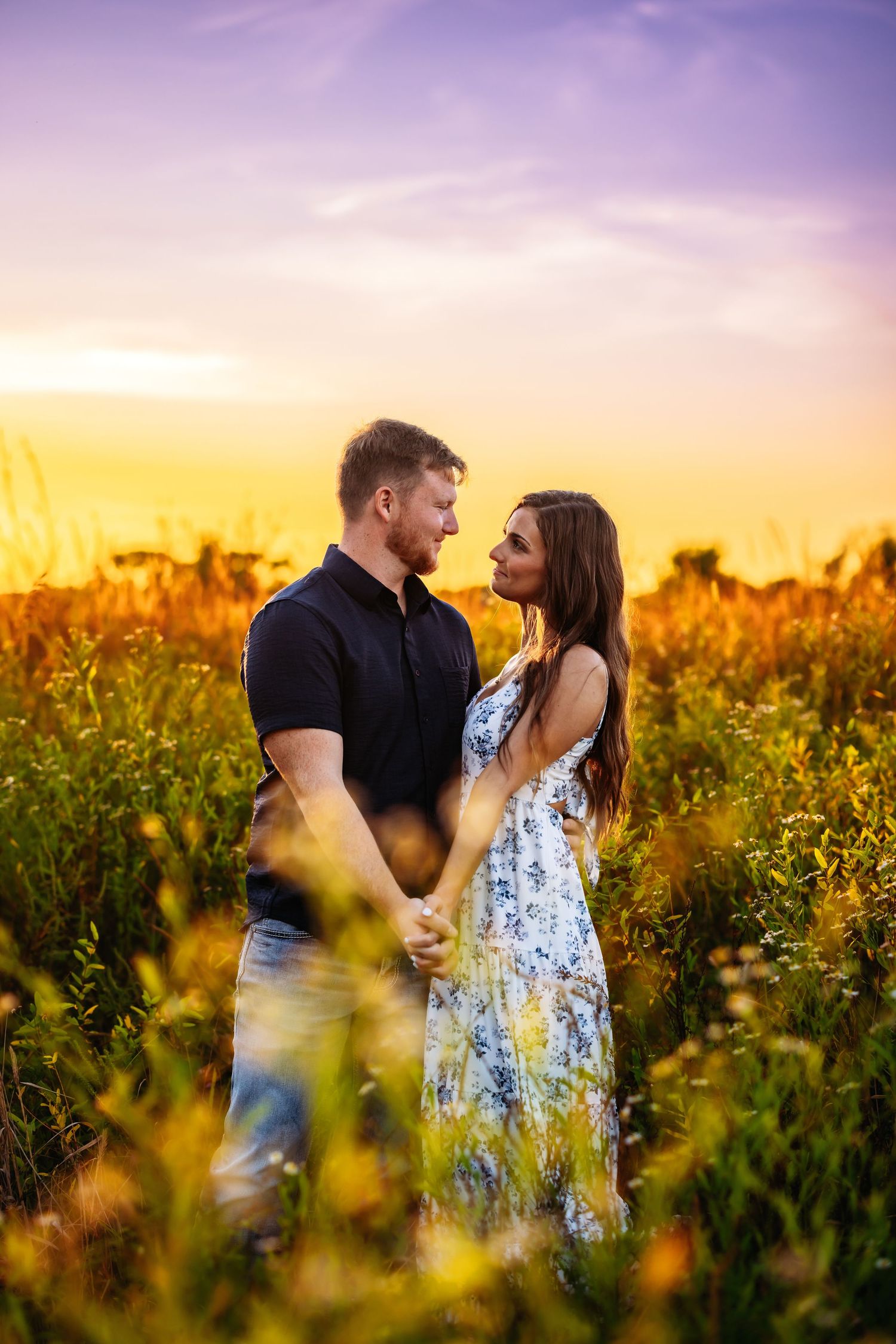 A romantic couple embraces in a golden field of wildflowers during a vibrant sunset.