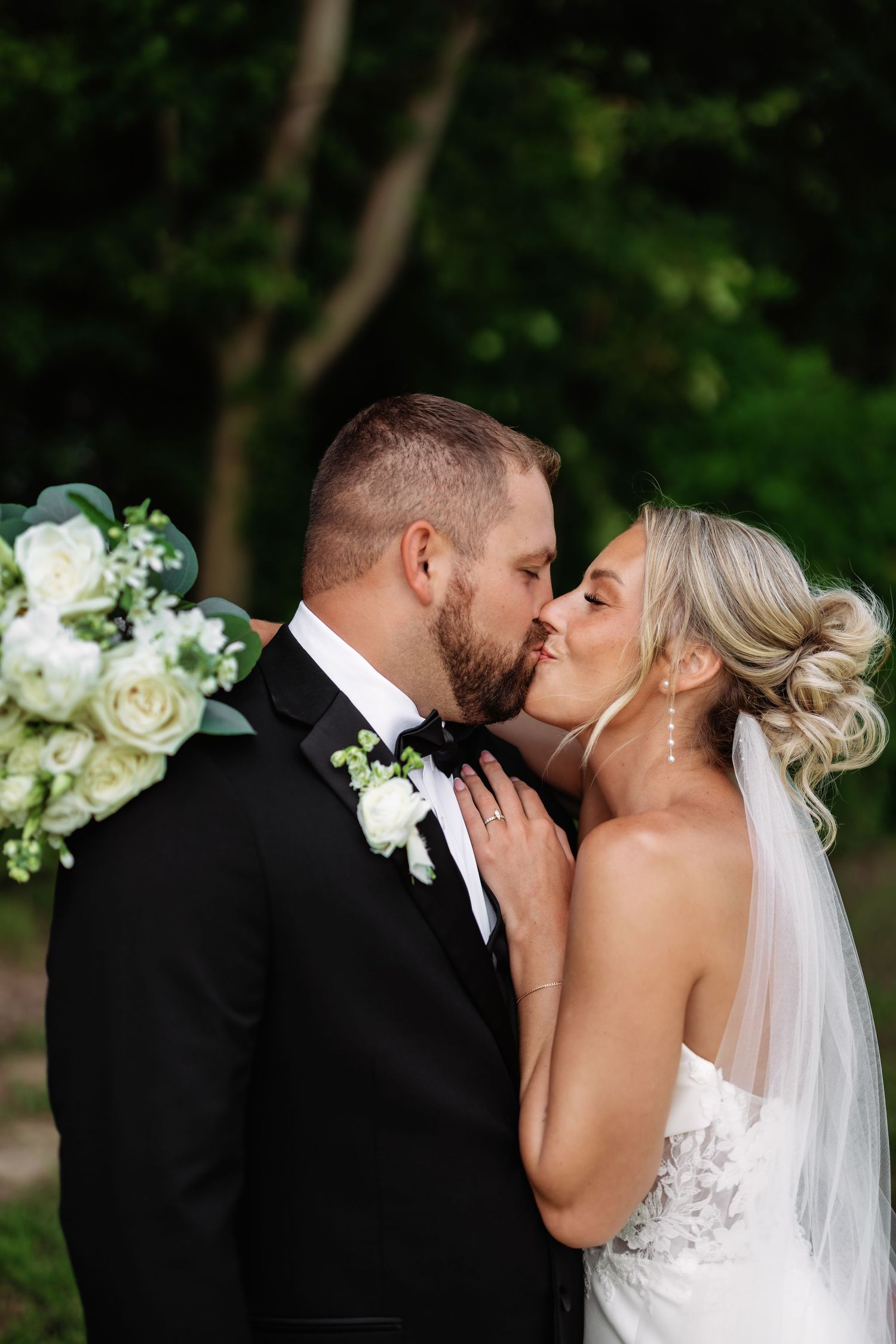 A romantic wedding moment captured outdoors with white roses and greenery in the background.