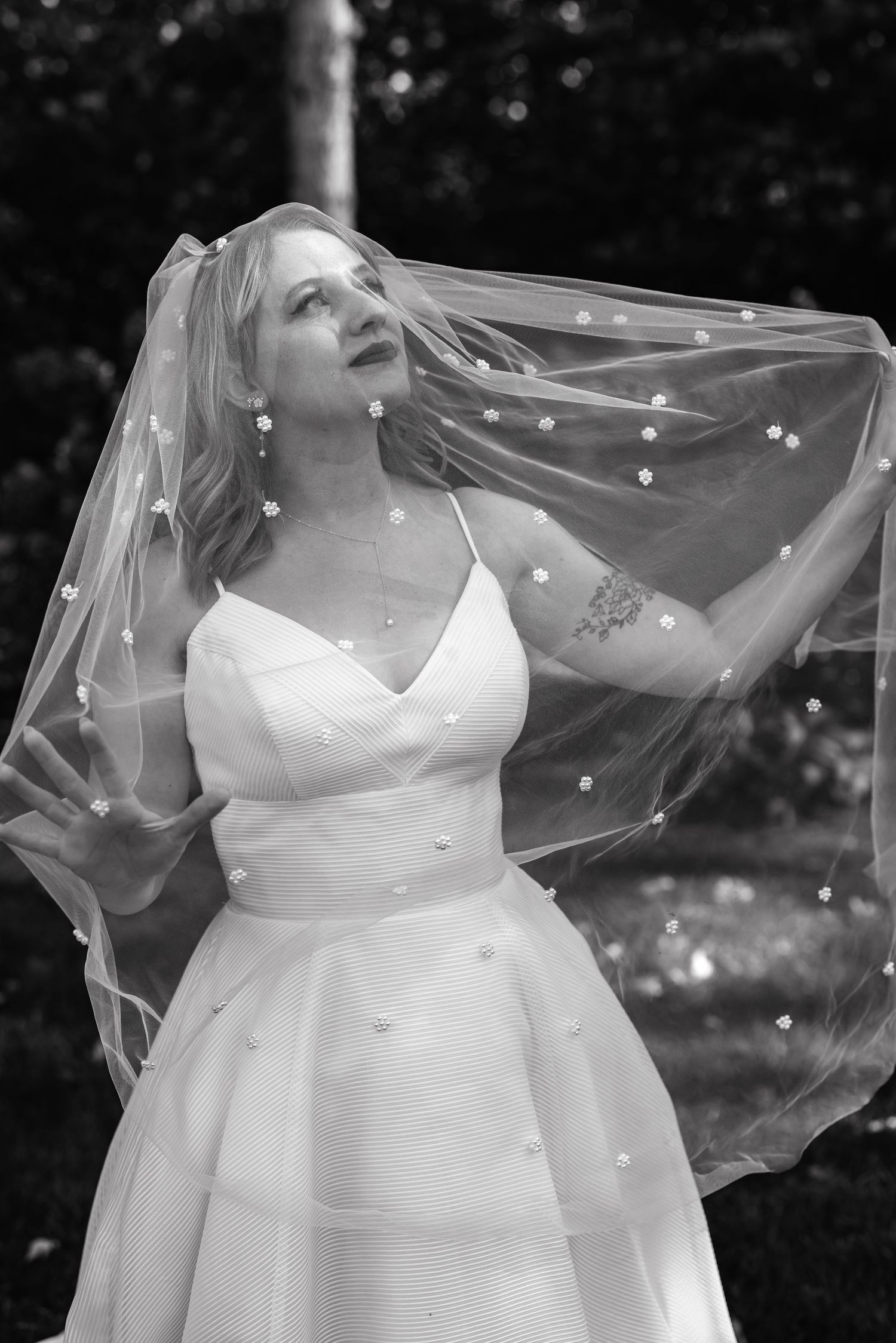 A bride in a classic white wedding dress looks up dreamily while her veil flows in the breeze.