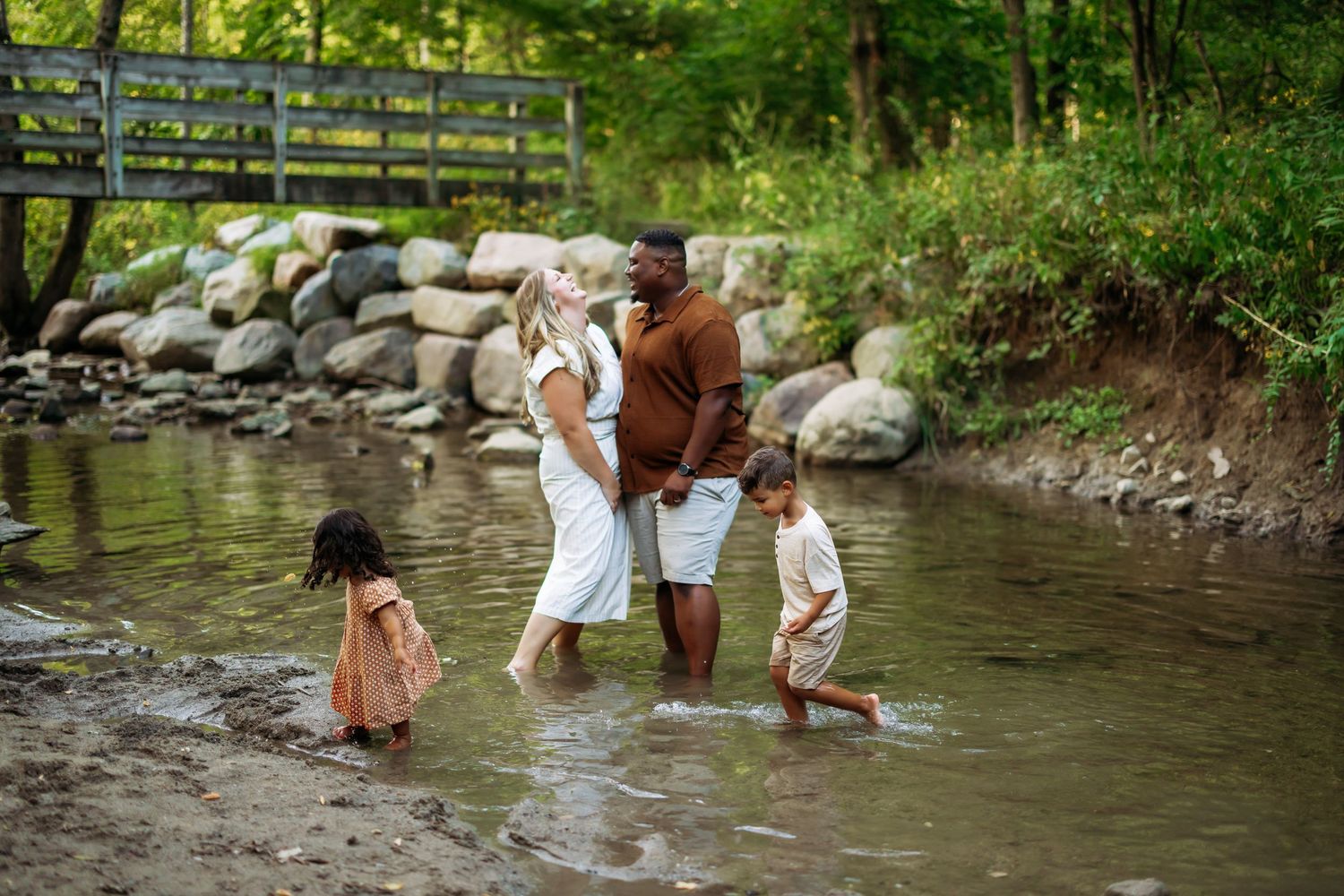 A group enjoys a summer day playing and splashing in a shallow creek surrounded by lush greenery.