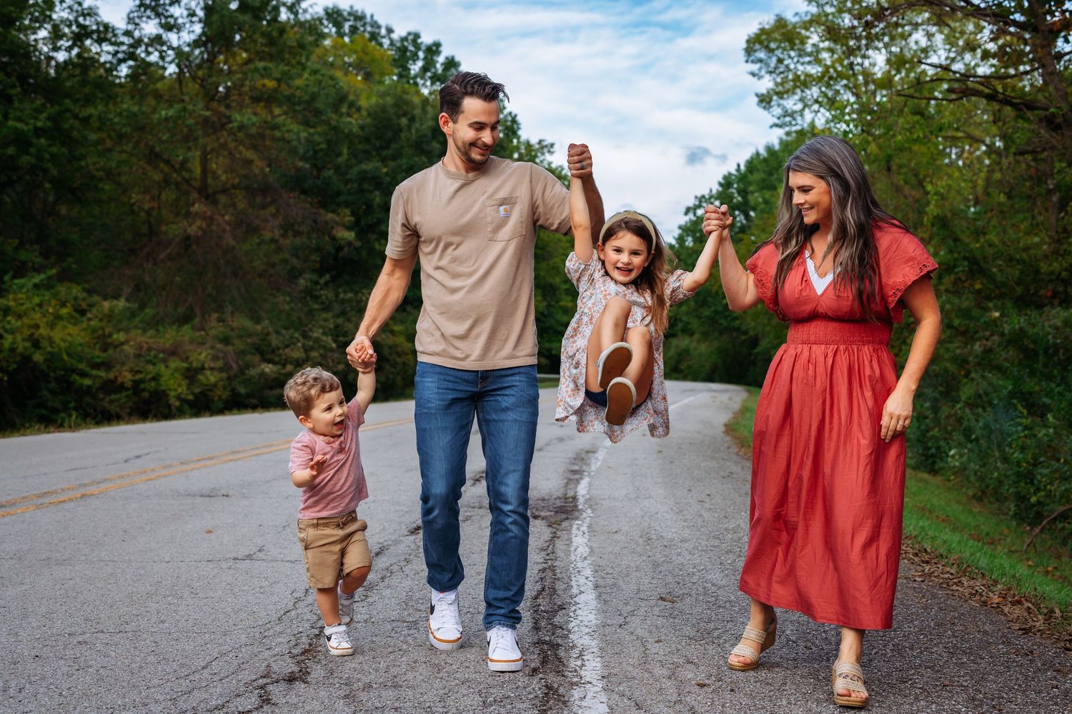 Family holding hands and walking together on rural road during autumn.