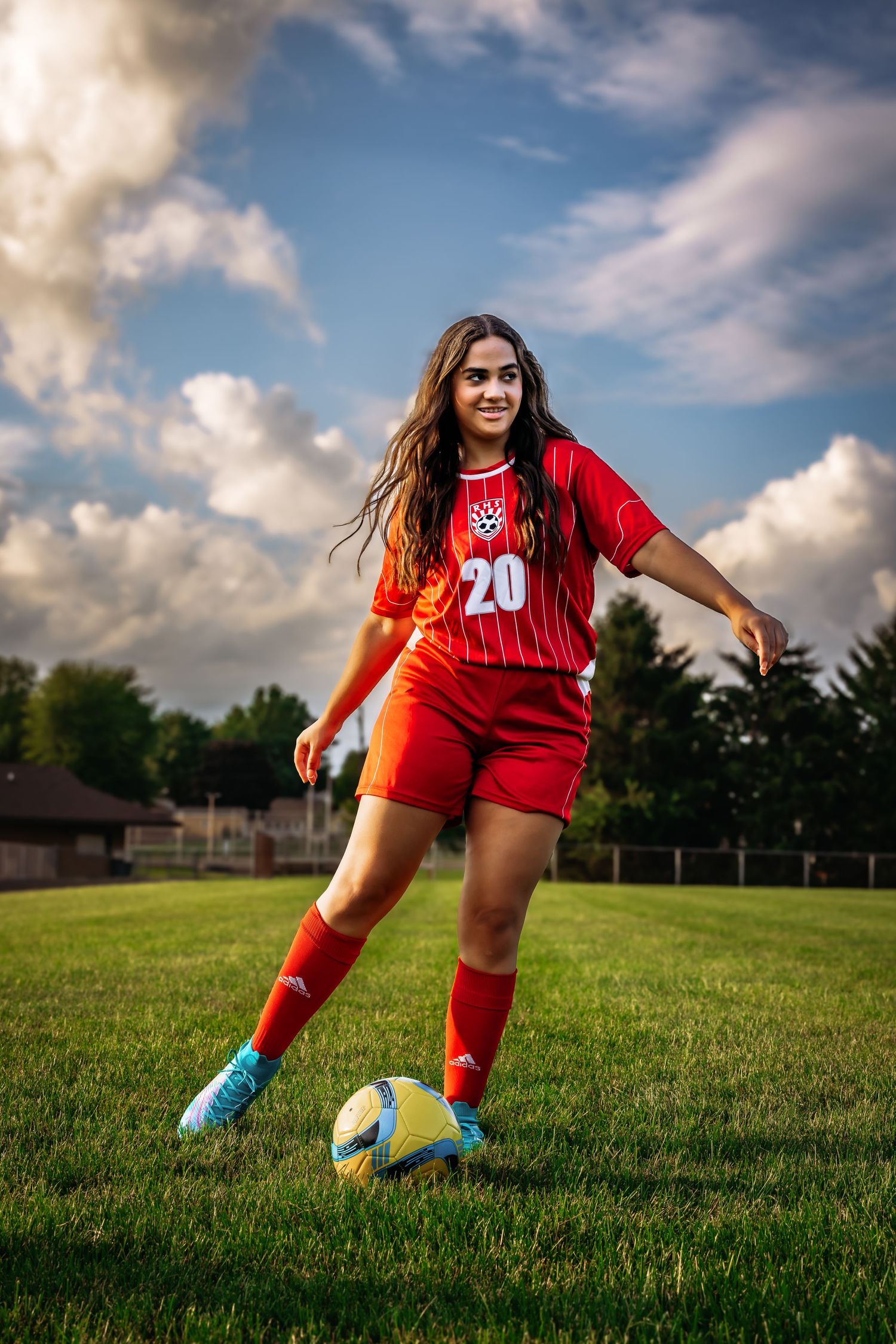 Female soccer player in red uniform practicing with ball on grass field during golden hour.