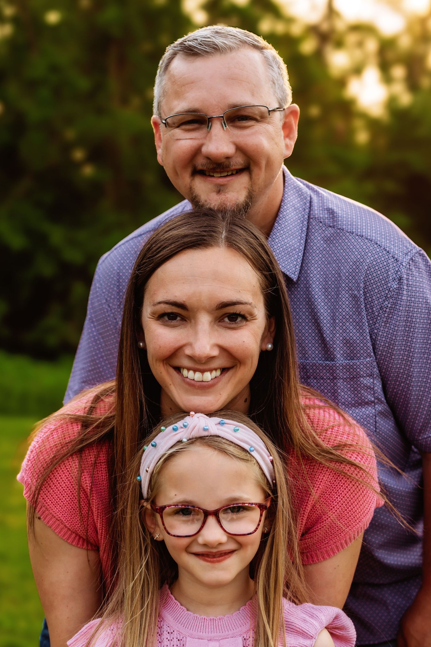 Family portrait outdoors at sunset featuring matching glasses and warm smiles in coral and purple clothing.