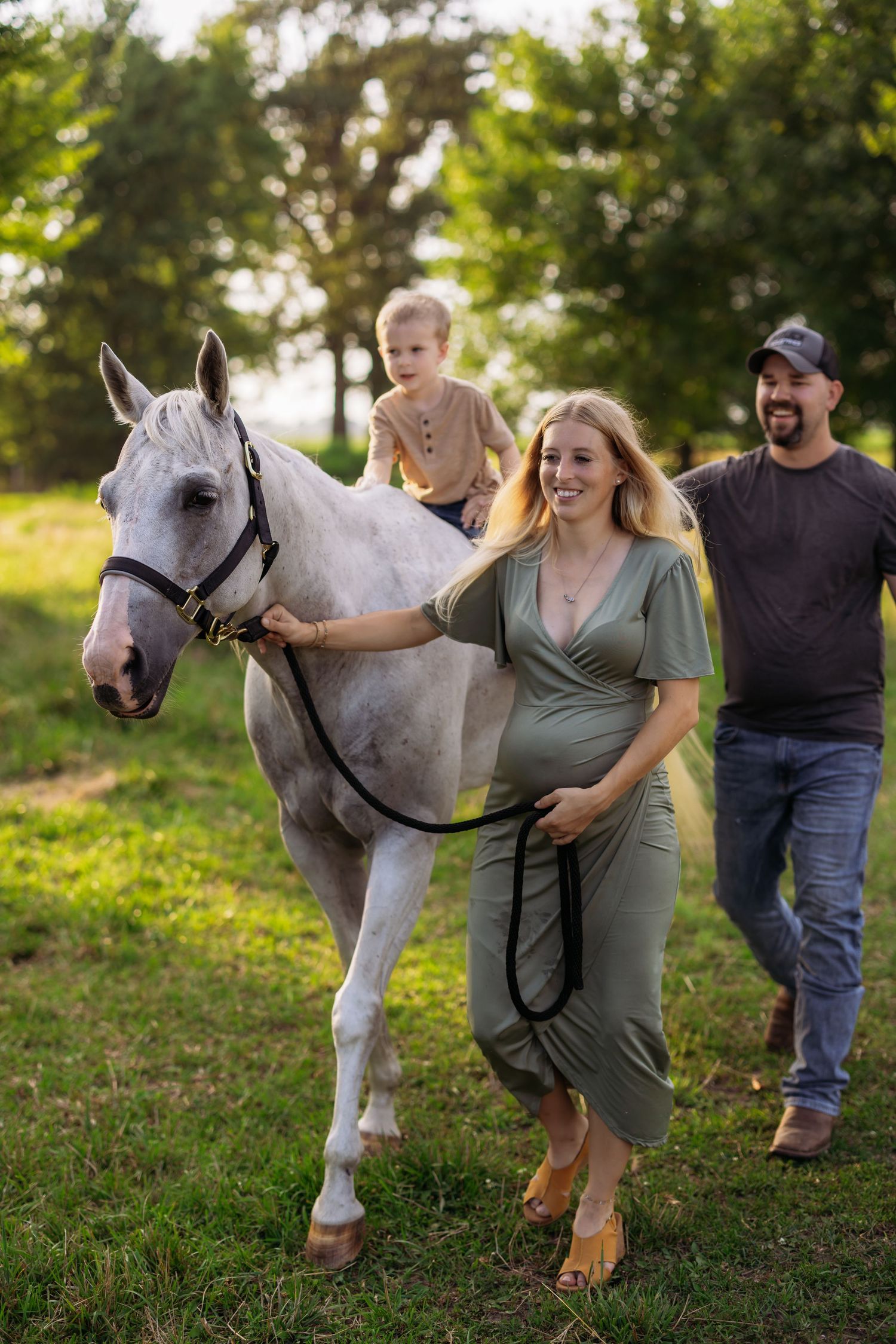 A couple walks with their beautiful white horse through a green grassy field on a sunny summer day.