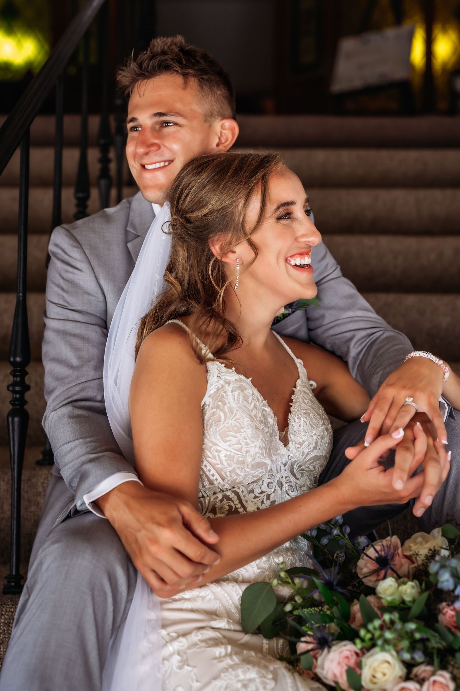 Happy newlyweds share joyful laughter while sitting on steps during wedding celebration.