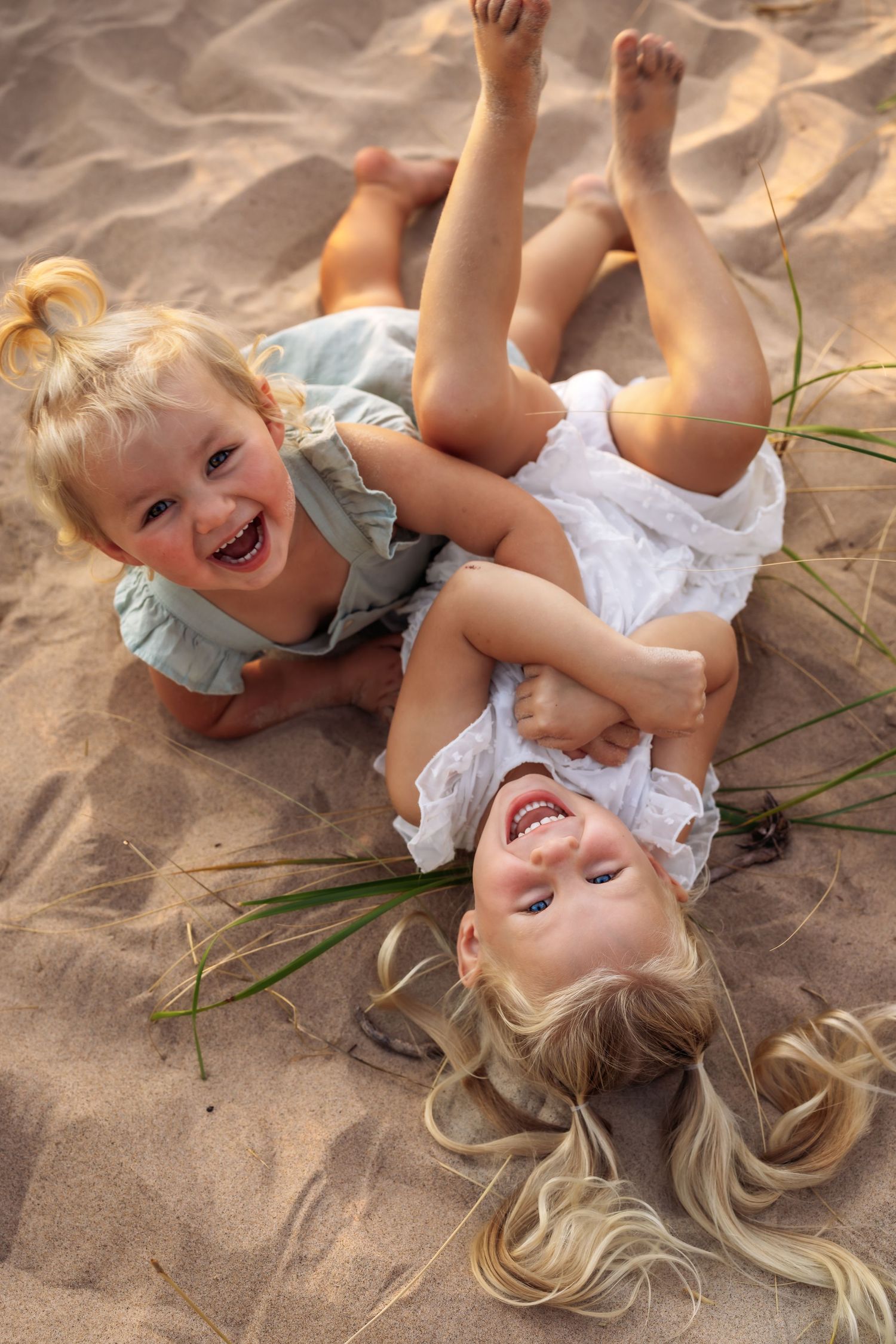 Two children playing and laughing while lying on sandy beach.