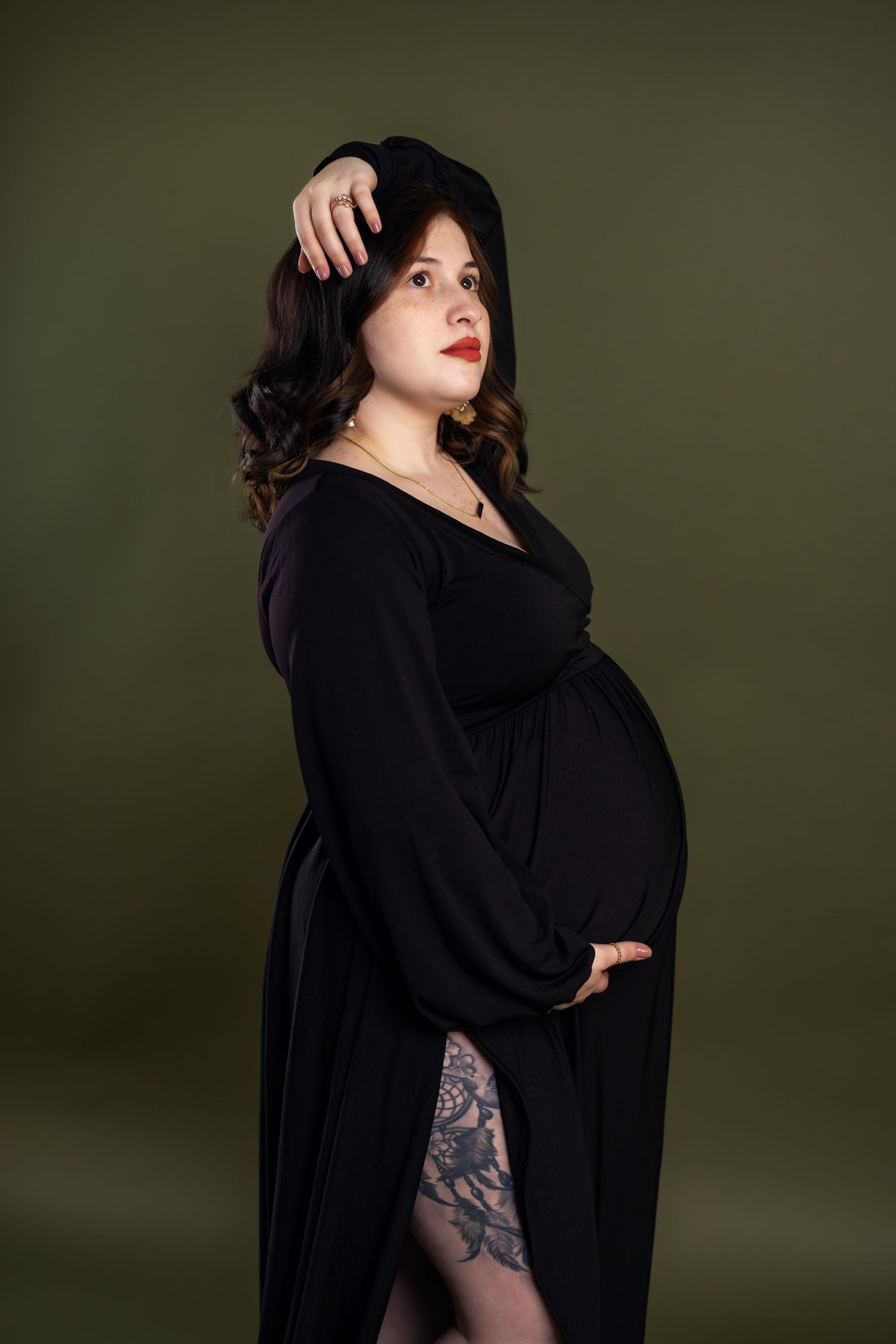 Maternity photo of woman in black dress against dark green background showing pregnancy silhouette.