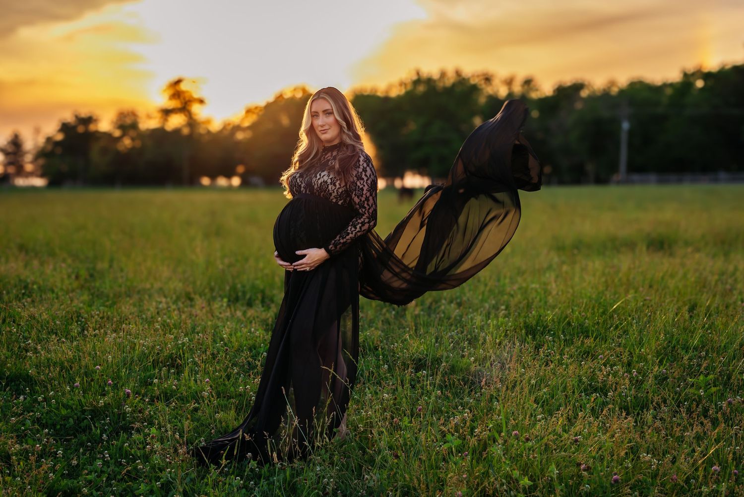 Maternity photo of woman in flowing black dress at sunset in field.