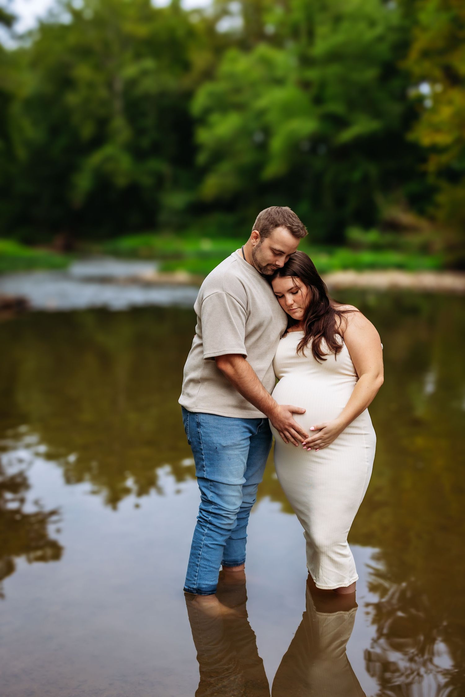 A couple shares a romantic moment while standing in shallow water by a lake on a summer day.