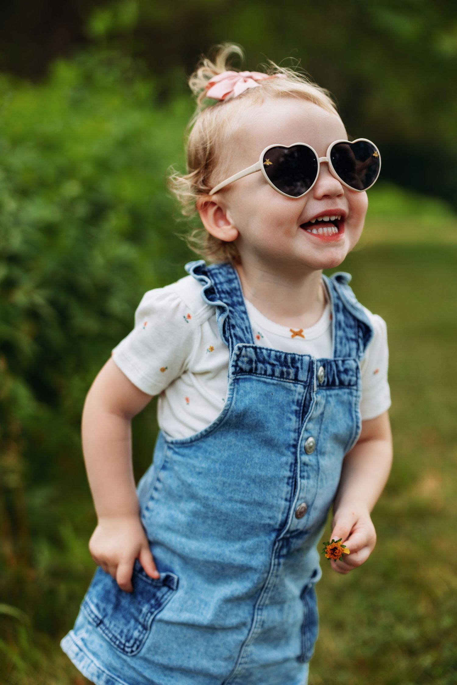 Toddler in denim overalls and heart sunglasses laughing outdoors.