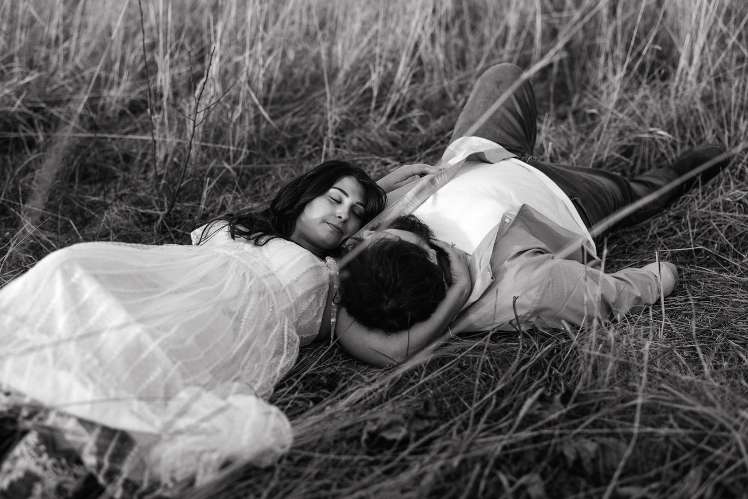 A couple lying together in tall grass while wearing white clothing and holding a rifle in this vintage black and white photo.