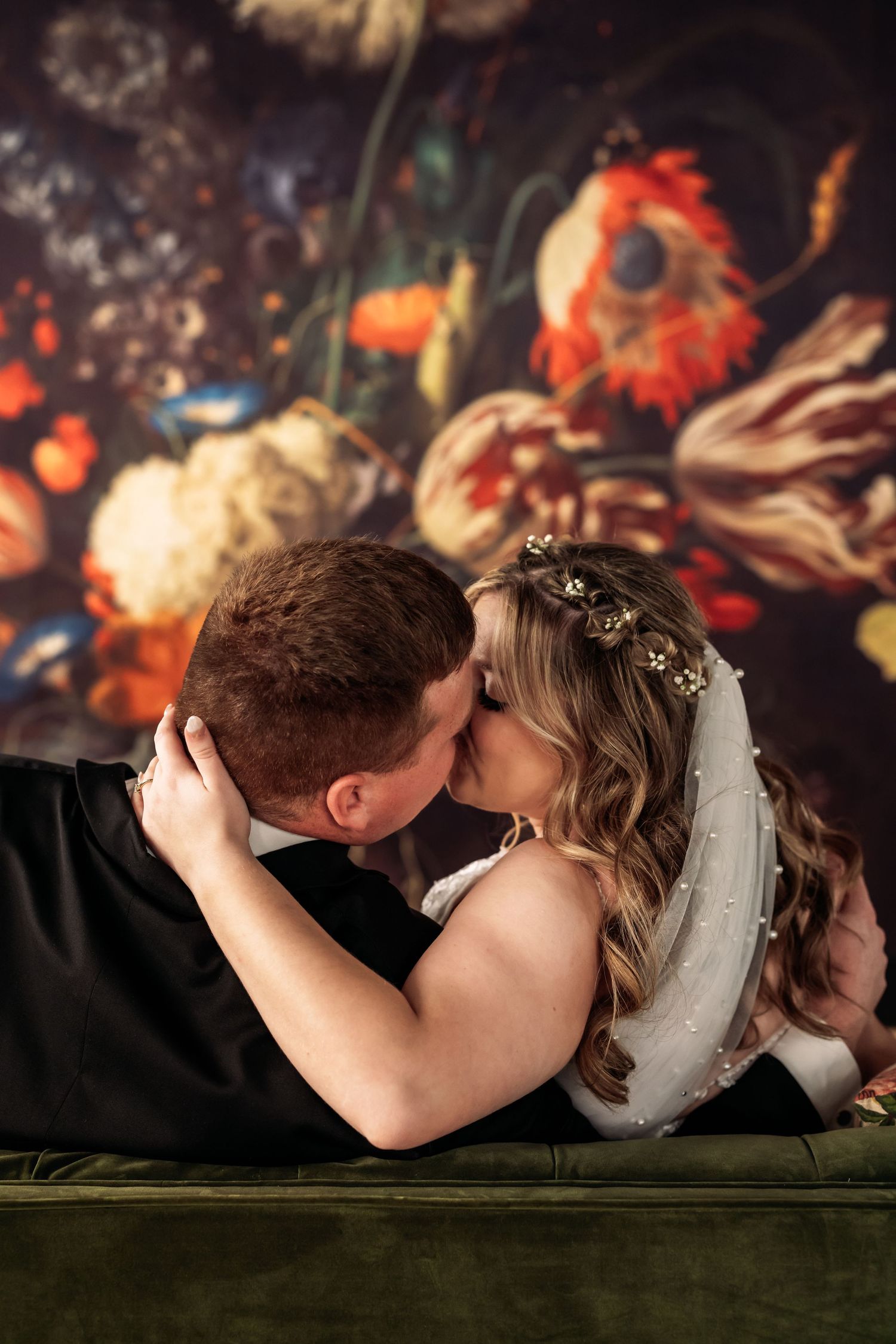 A romantic wedding portrait with couple kissing against vintage floral painting backdrop.
