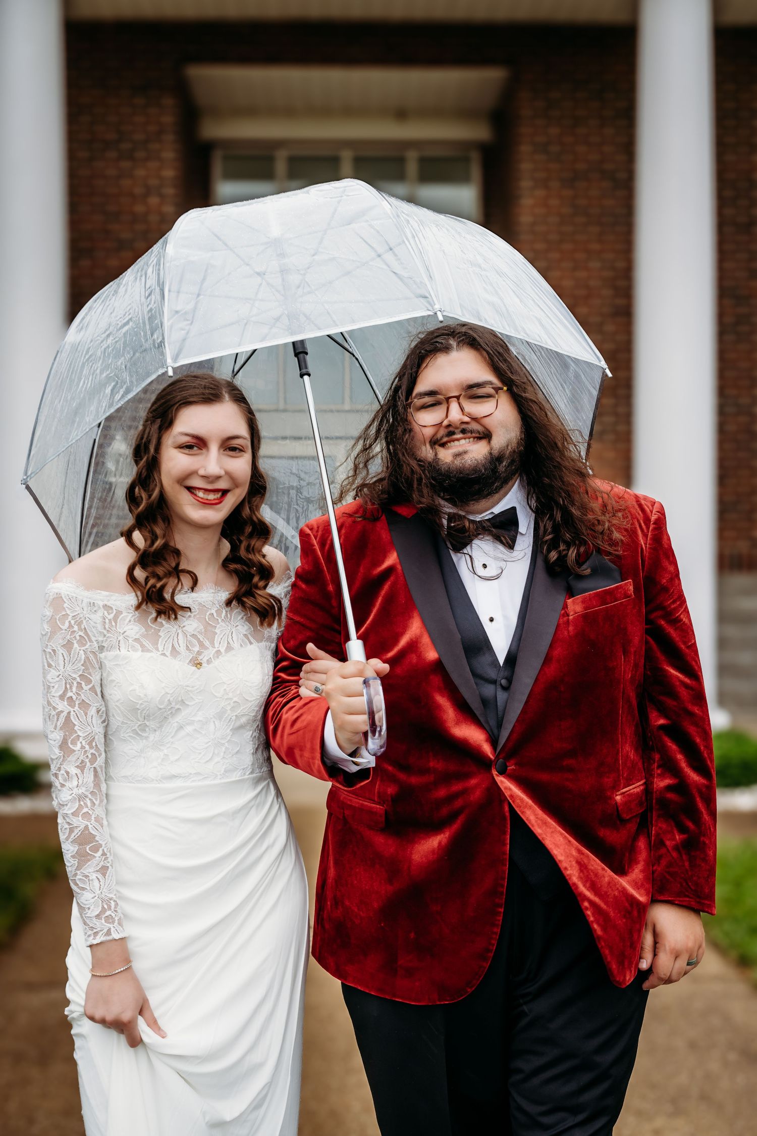 A wedding couple shares an umbrella in front of a church entrance on their special day.