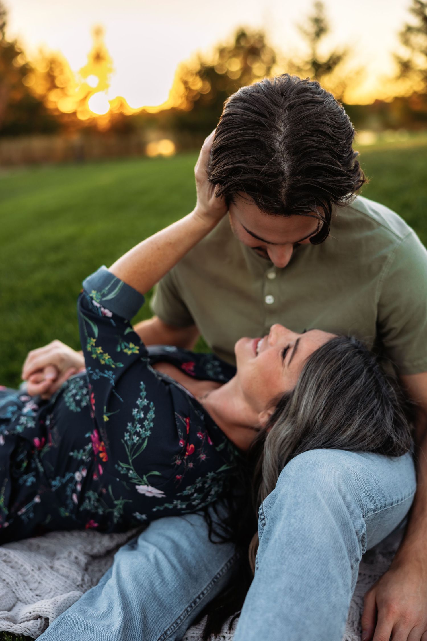 A couple shares an intimate moment while laying together at sunset in a grassy field.