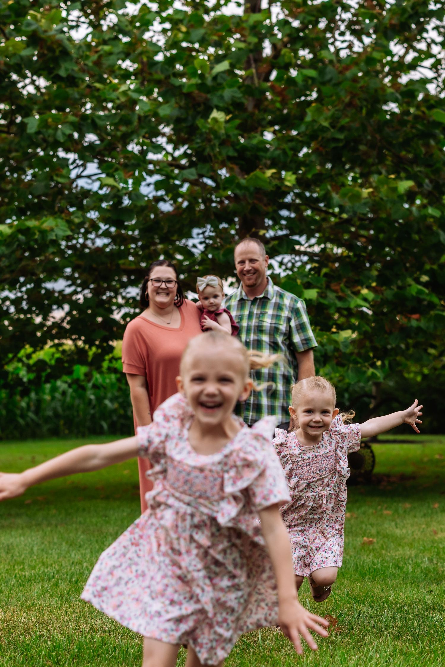 Young children run and play energetically on a green lawn with trees in the background on a sunny day.