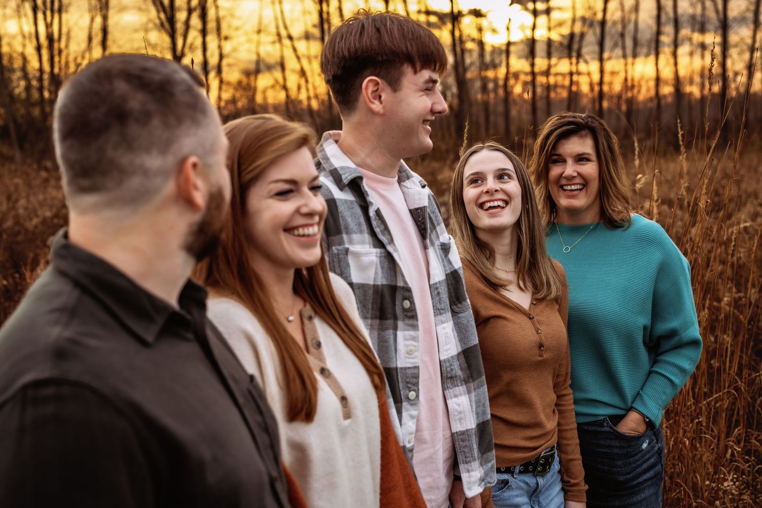 Group of friends laughing together during golden hour sunset in a field.