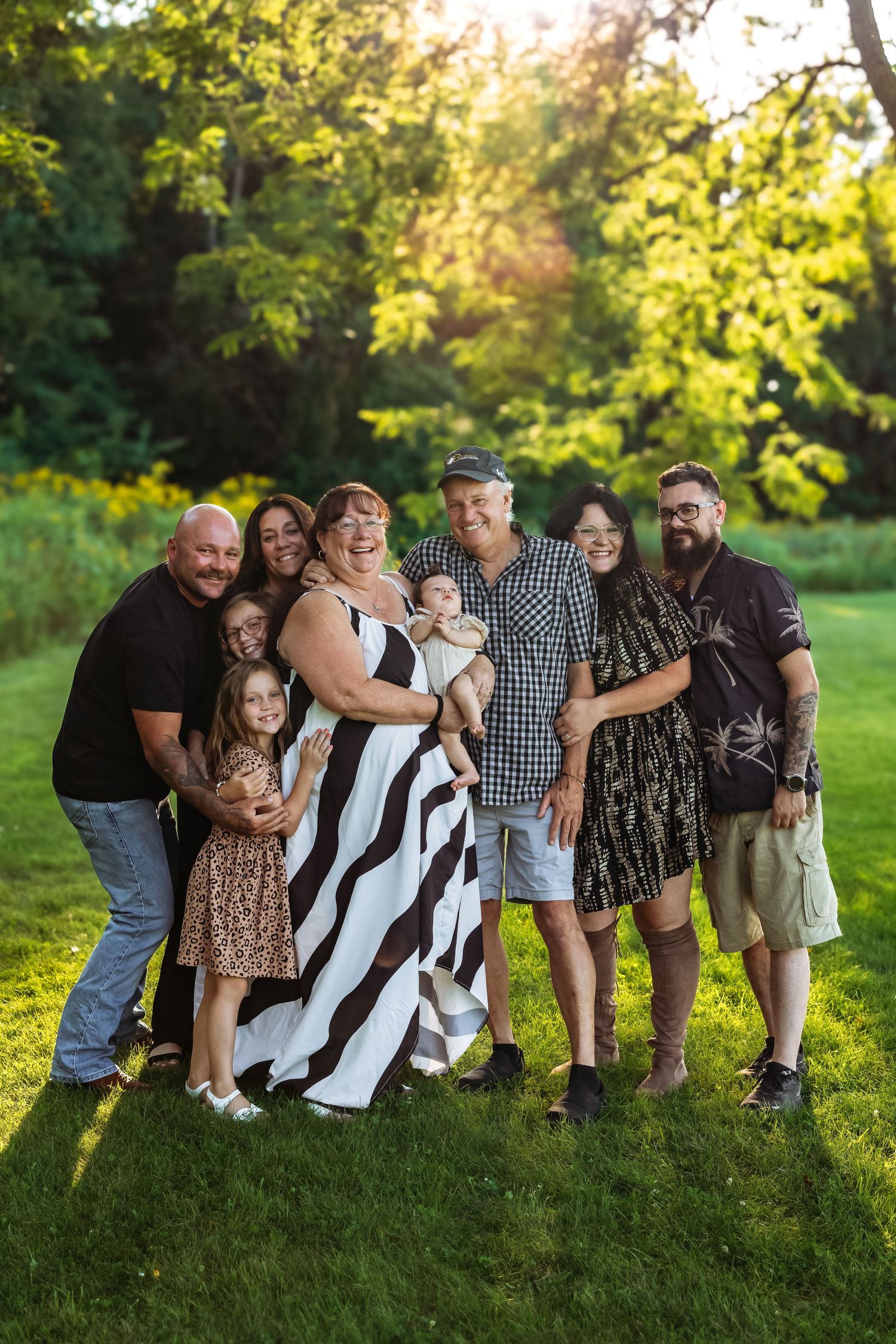Large family group poses together for portrait in lush green outdoor setting during golden hour.