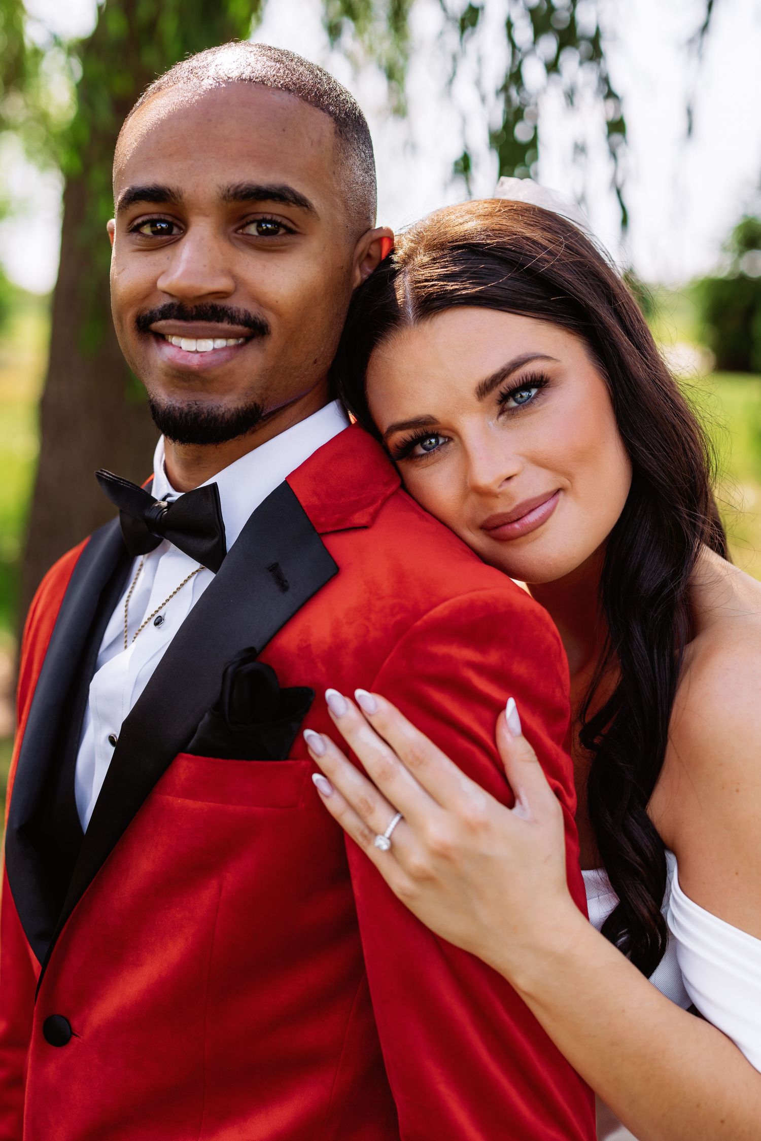 A joyful wedding portrait featuring a couple in a striking red tuxedo and white gown.