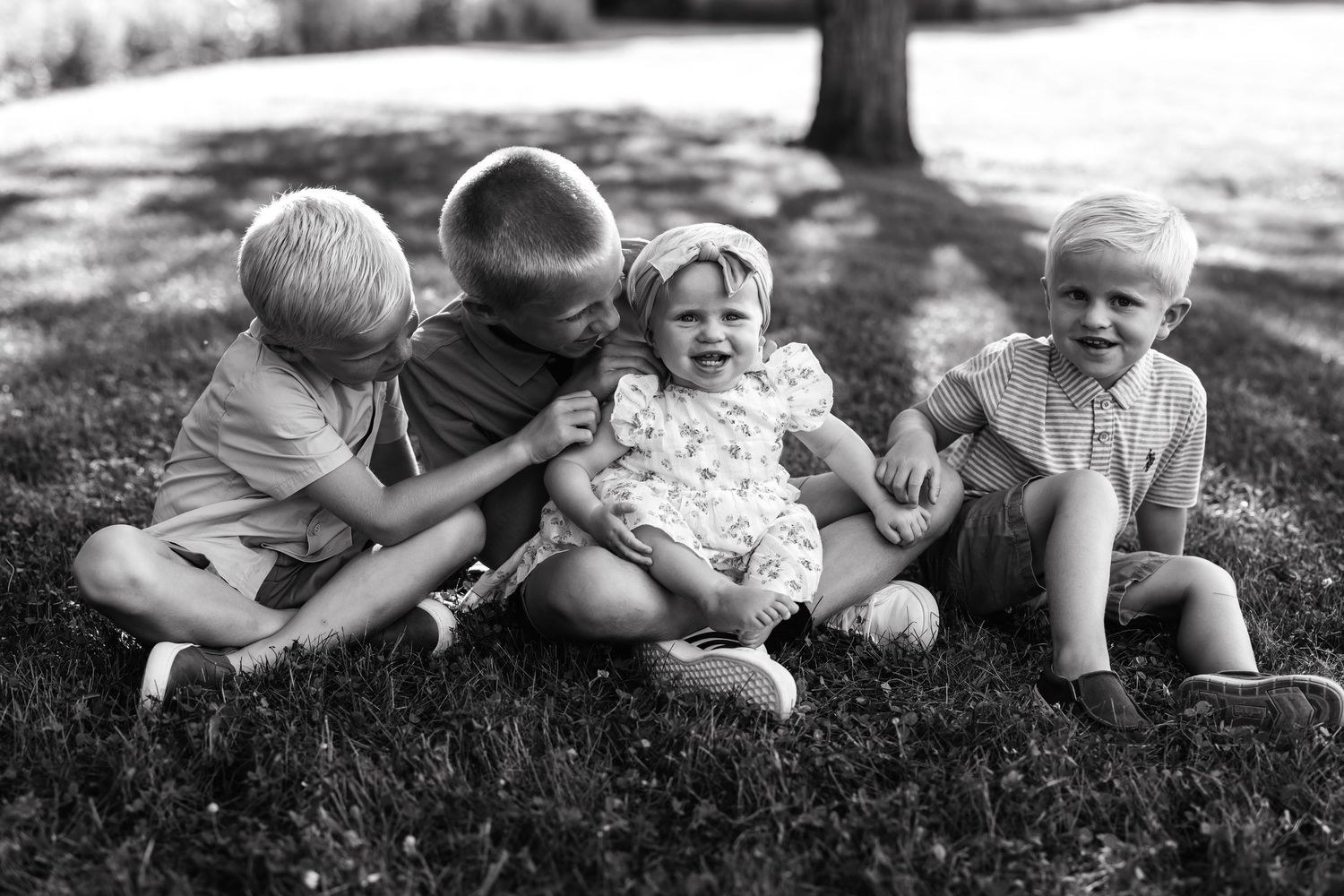 Vintage black and white photograph of four small children sitting together on grass in summertime.
