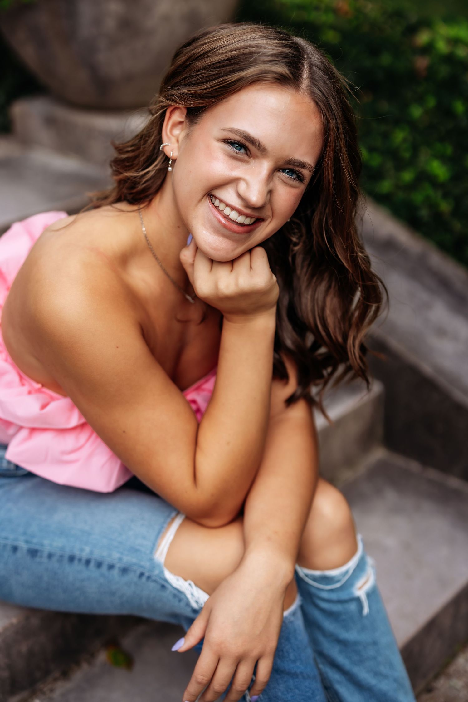 Casual portrait of someone in pink top and jeans sitting on concrete steps outdoors.