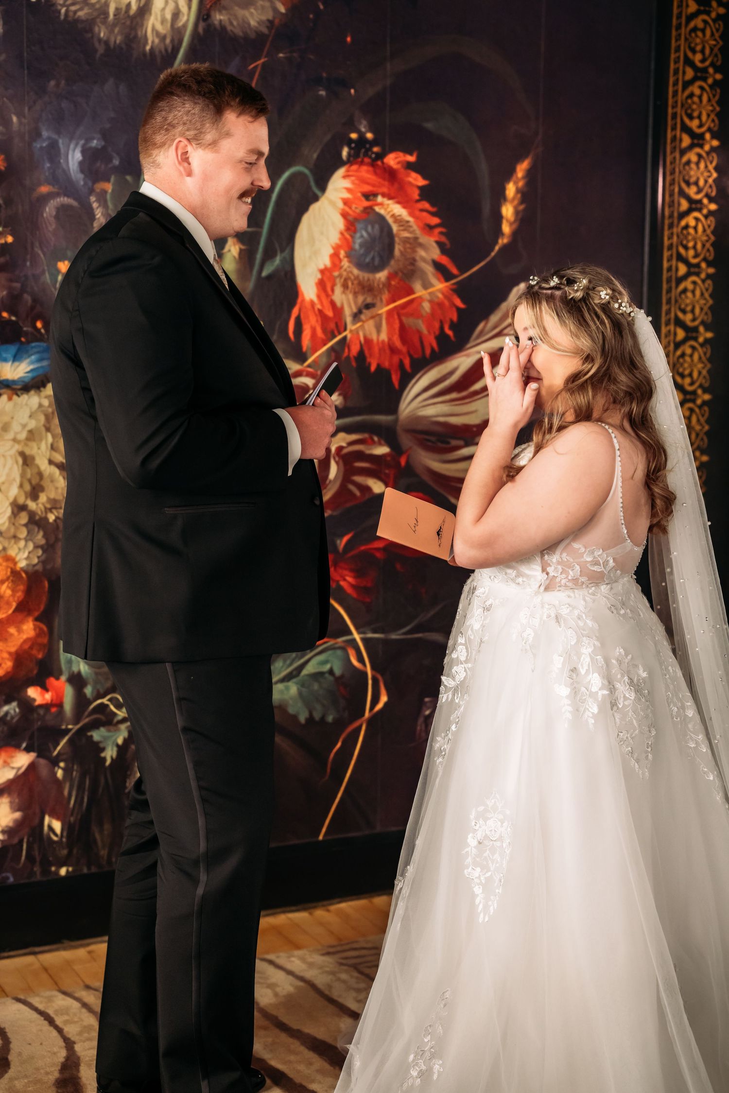 Wedding couple shares a lighthearted moment in front of a vibrant rooster painting.
