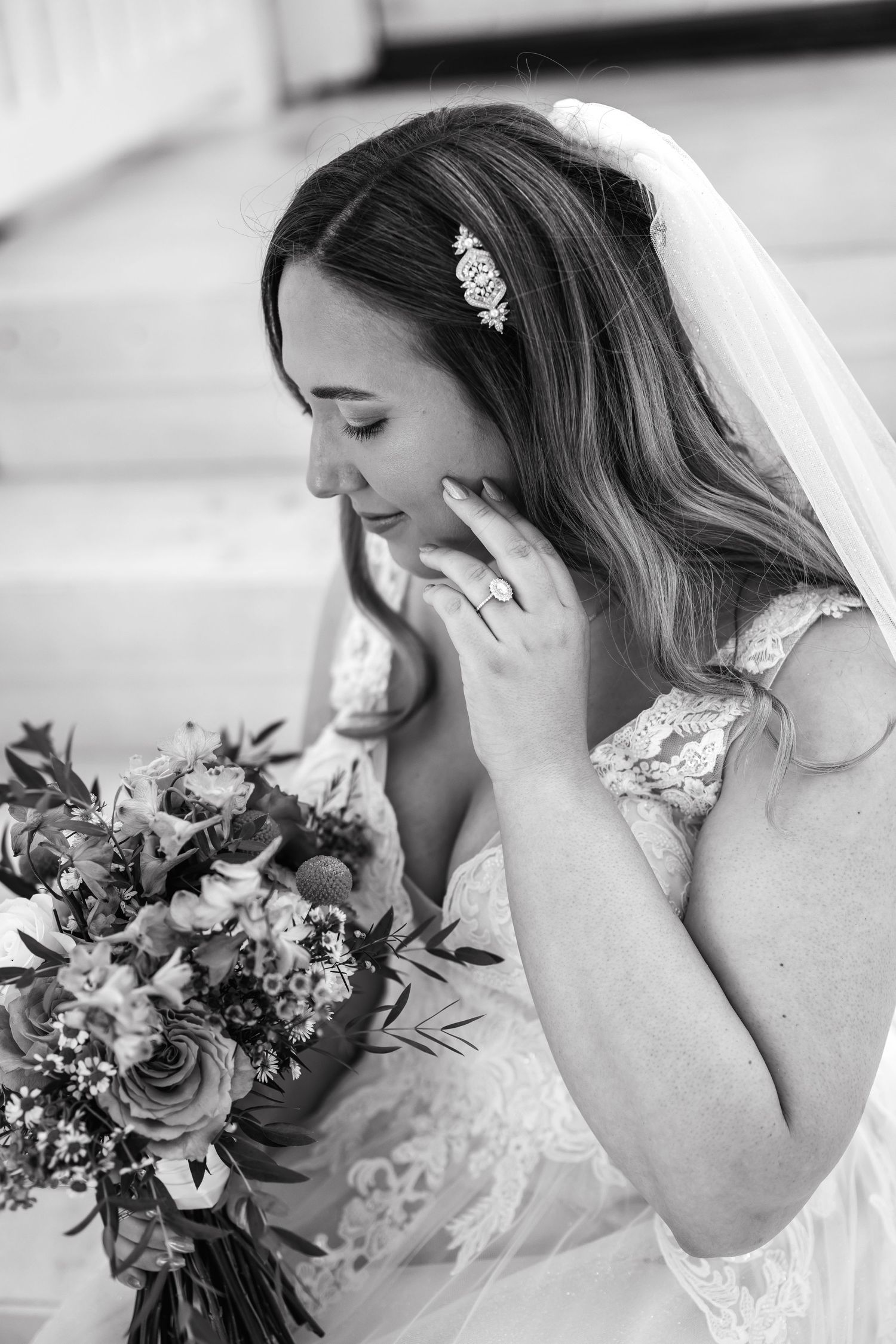 Emotional bride in lace dress holds bouquet while covering mouth during wedding moment.