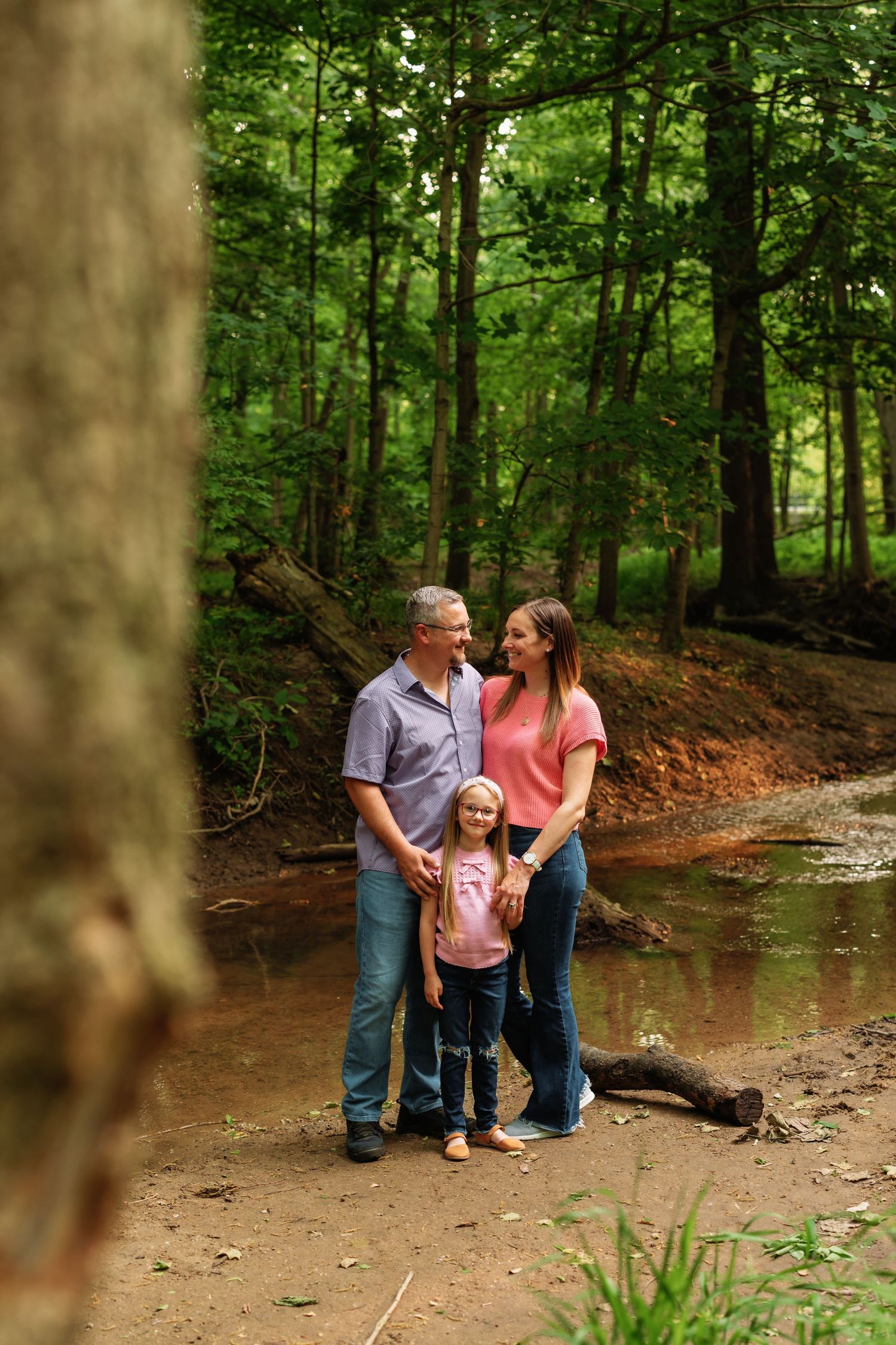 A family shares a tender moment while sitting together on a fallen tree in a lush forest setting.