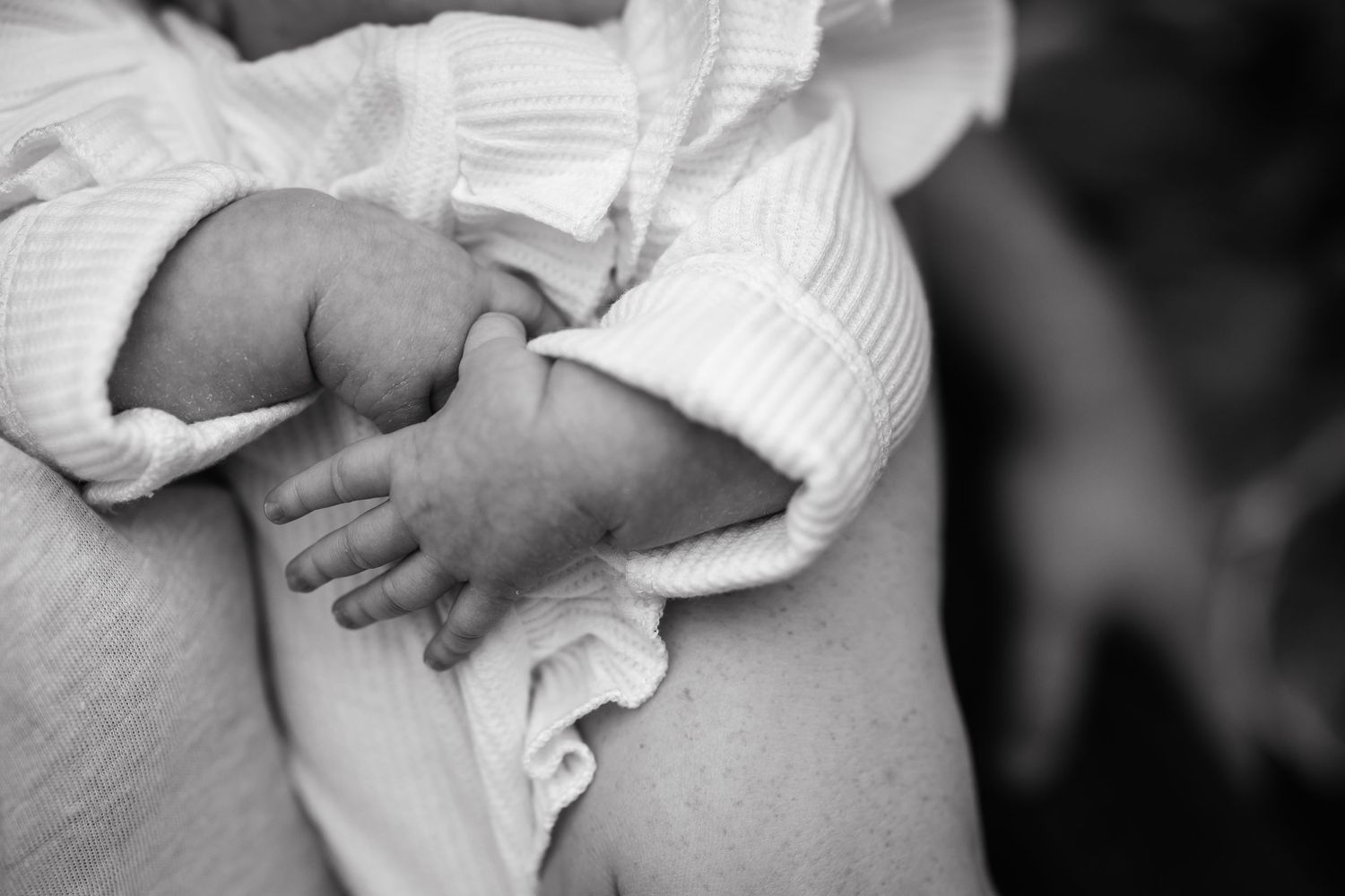 A black and white close-up of a baby's tiny hand grasping white fabric.