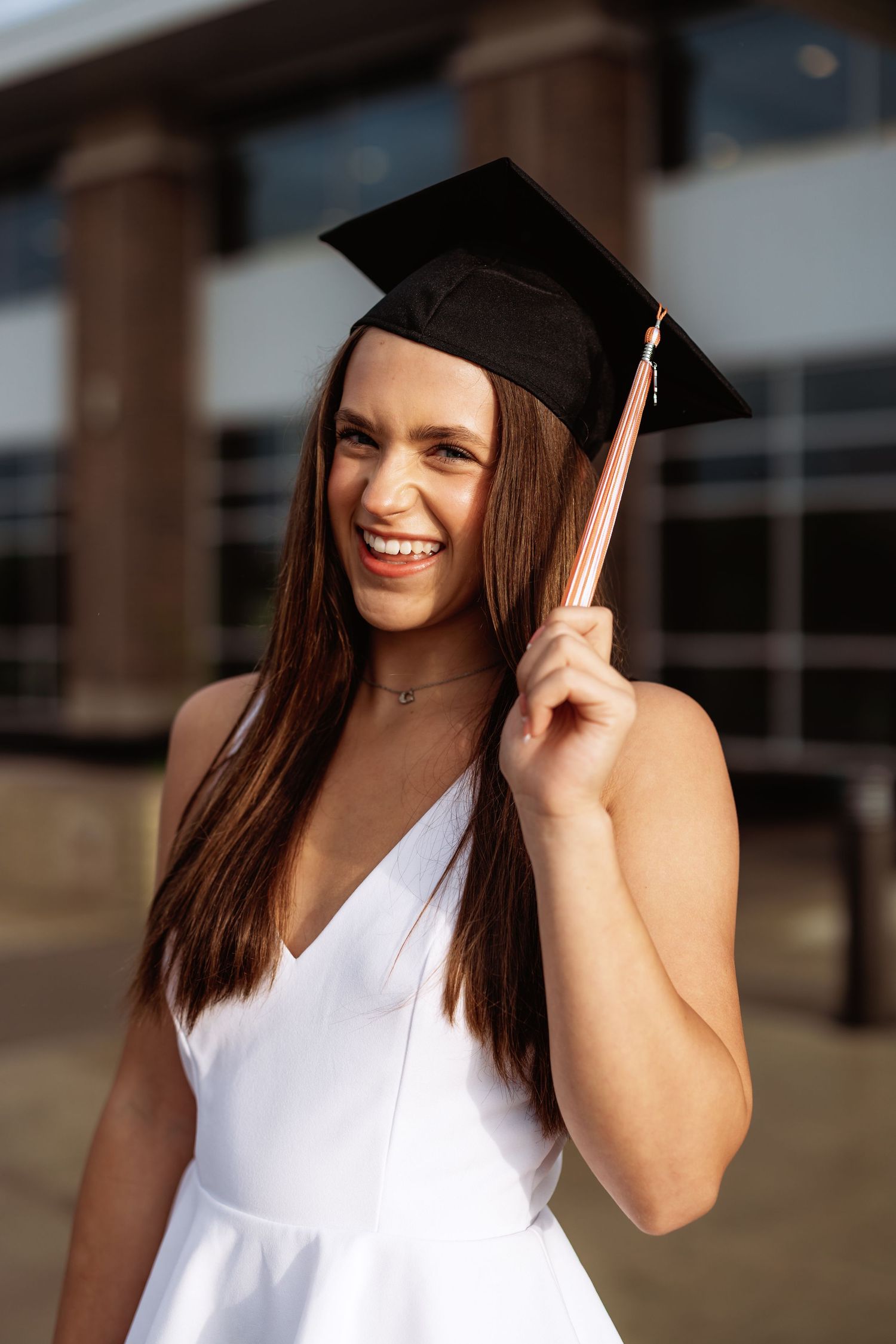 Graduate in white dress and cap poses with bright smile.