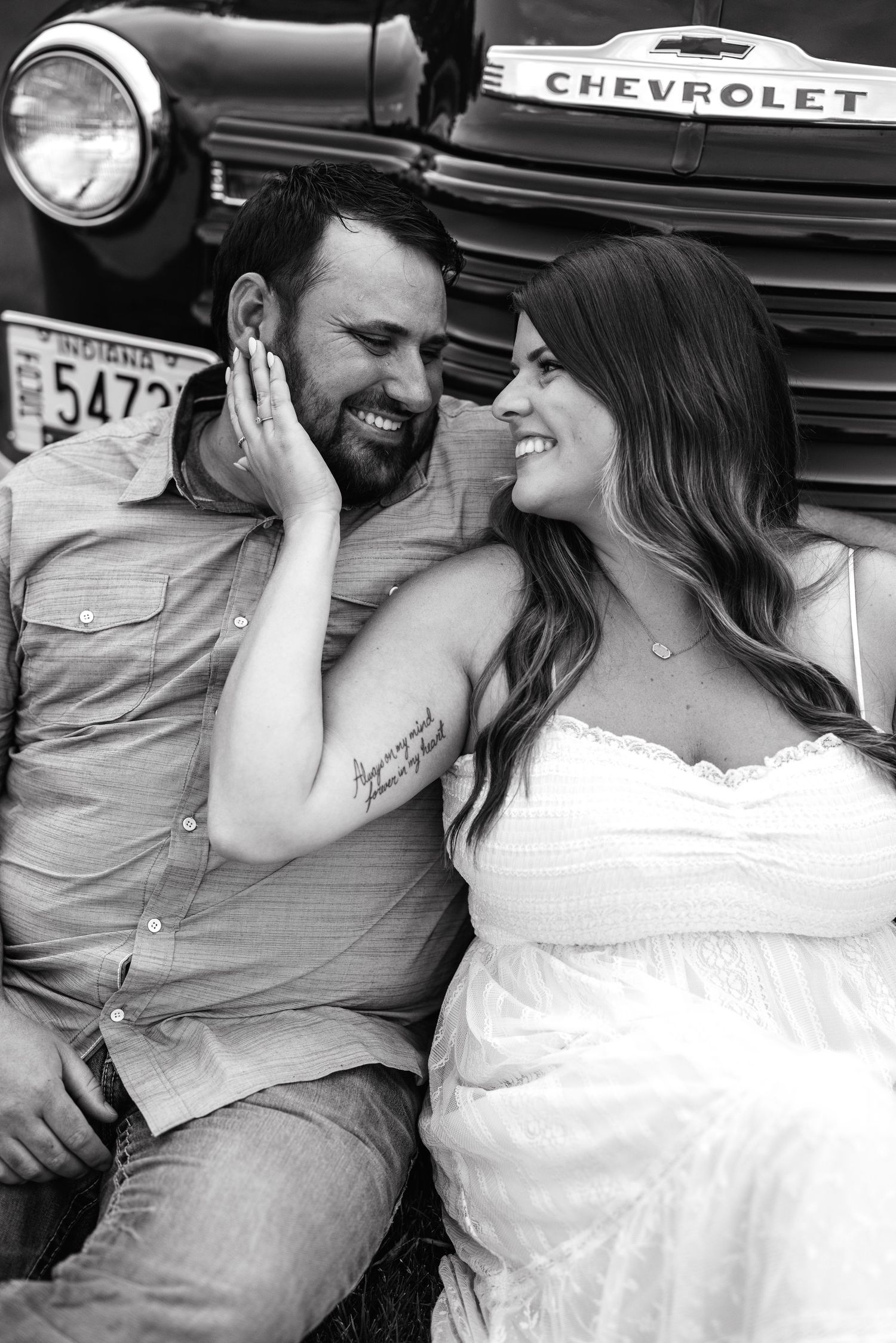 A romantic black and white portrait of a couple sitting beside a vintage Chevrolet truck.