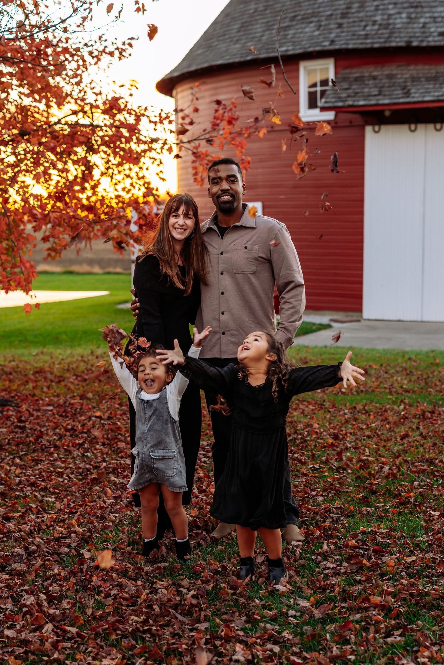 Family enjoying autumn scenery in front of red barn as leaves fall.