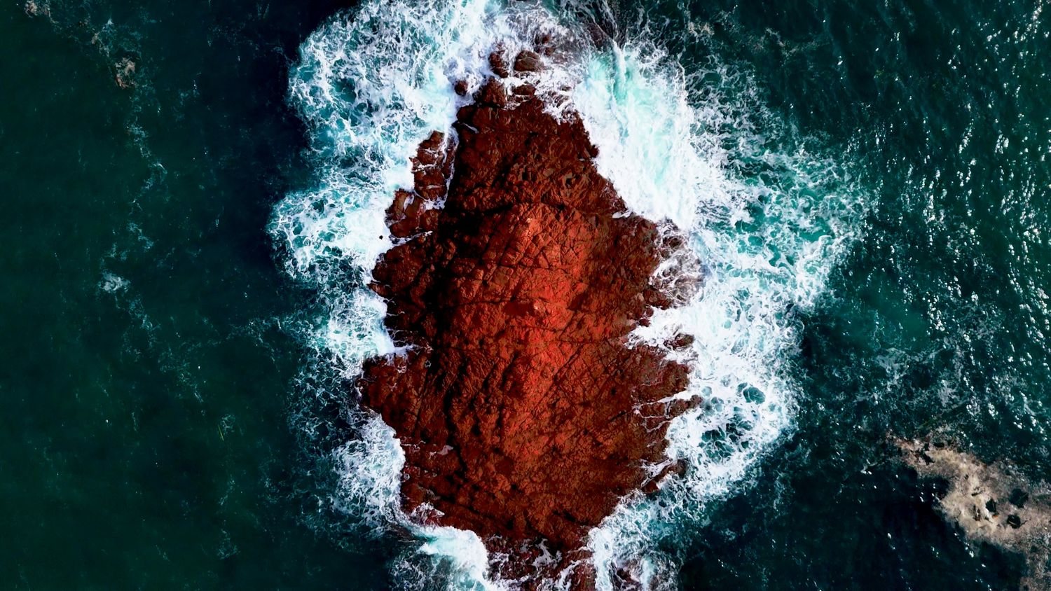 Photographie aérienne par drone d’un îlot rocheux entouré de vagues, captée par Mathieu Breton.