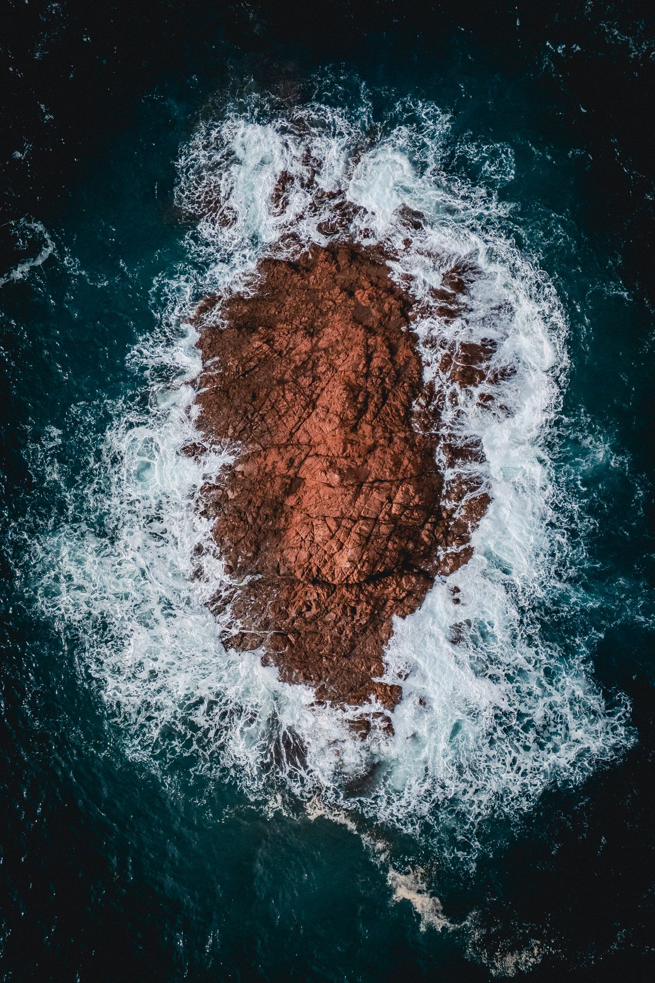 Photographie aérienne artistique d’une roche battue par les vagues en mer, captée par le photographe Mathieu Breton.