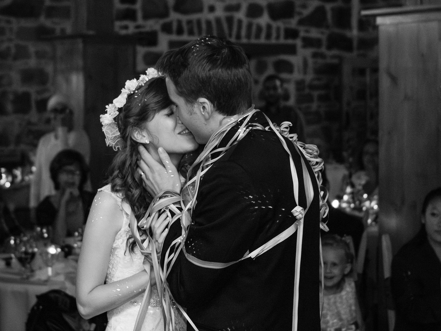 Photographie de mariage en noir et blanc par Mathieu Breton : baiser des mariés entourés des invités.
