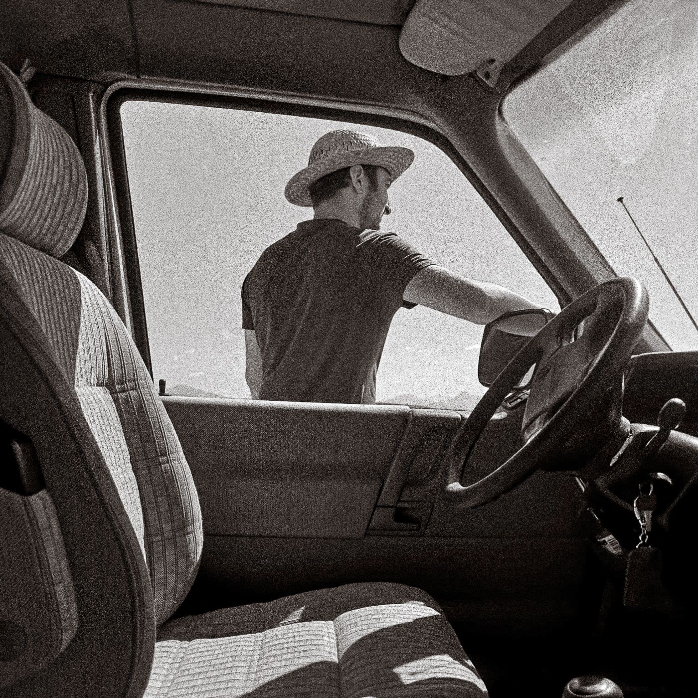 Photographie artistique en noir et blanc d’un homme portant un chapeau vu de dos dans un camion, réalisée par le photographe Mathieu Breton.