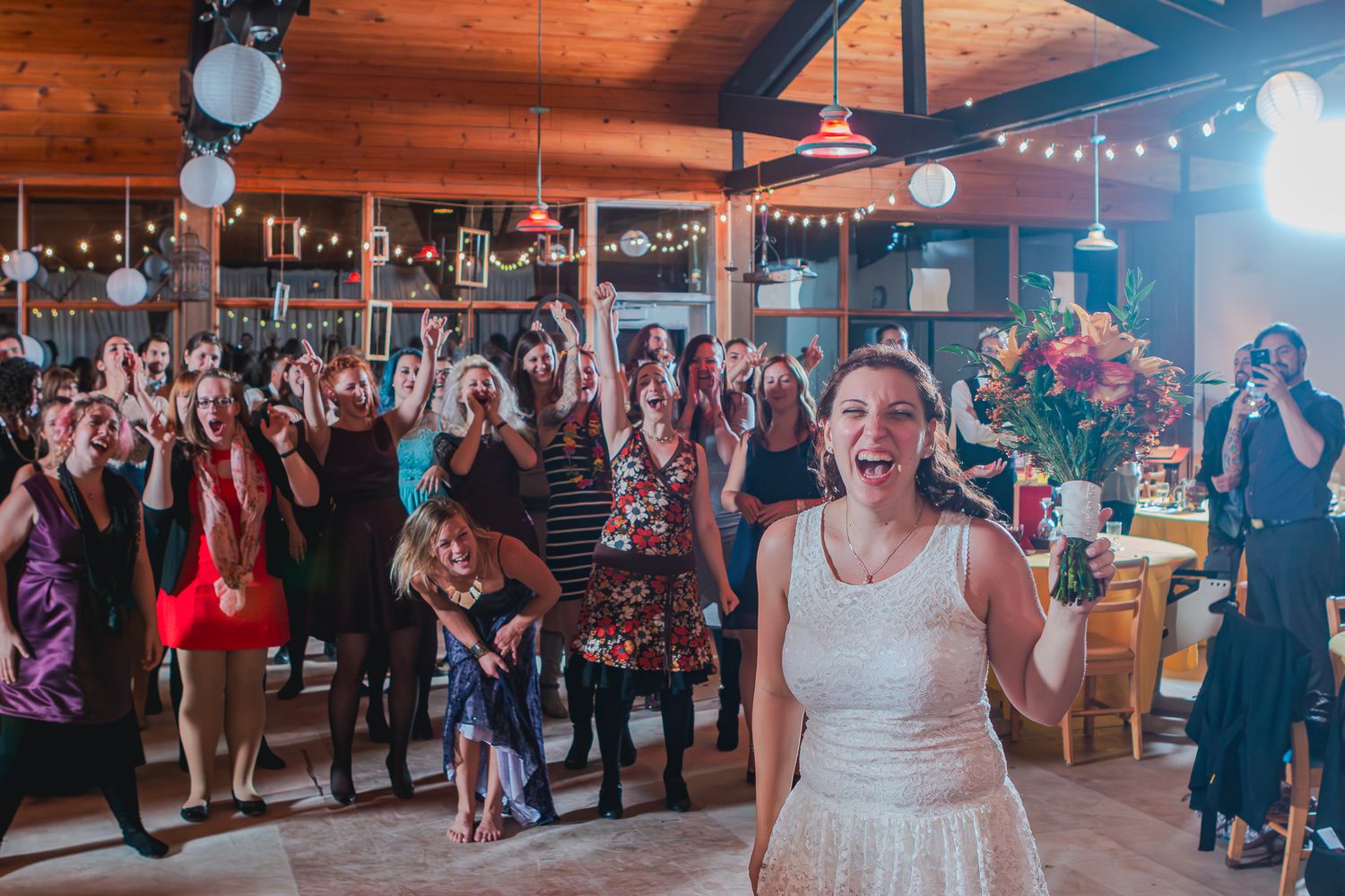 Photographie de mariage par Mathieu Breton : Geneviève prête à lancer son bouquet devant ses invitées.