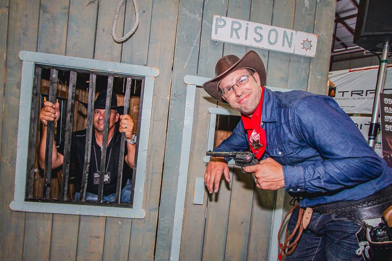 Portrait de Rudy, réalisé par le photographe Mathieu Breton, devant une façade en bois décorée d’une pancarte “Prison”.