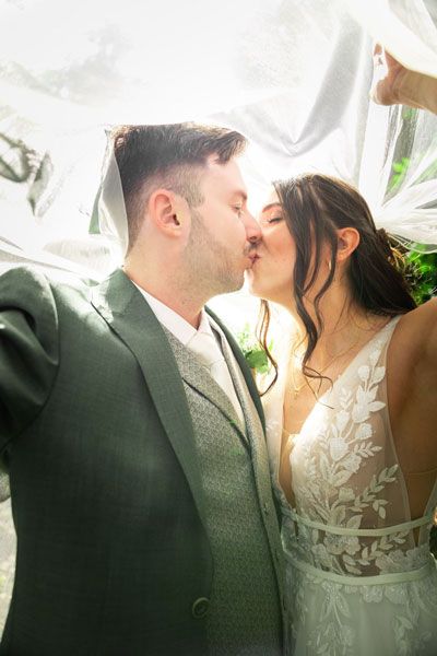 Bride and groom sharing a romantic kiss under a flowing white veil on their wedding day.