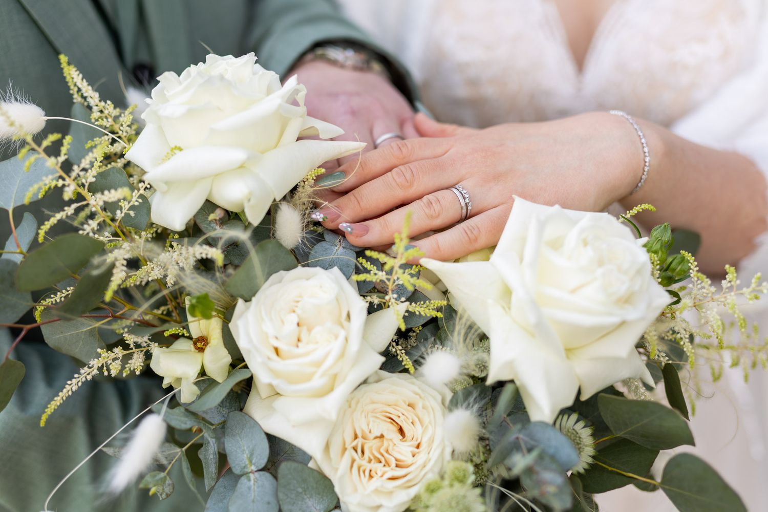 Newlyweds display wedding rings on a bridal bouquet of white roses and eucalyptus greenery.