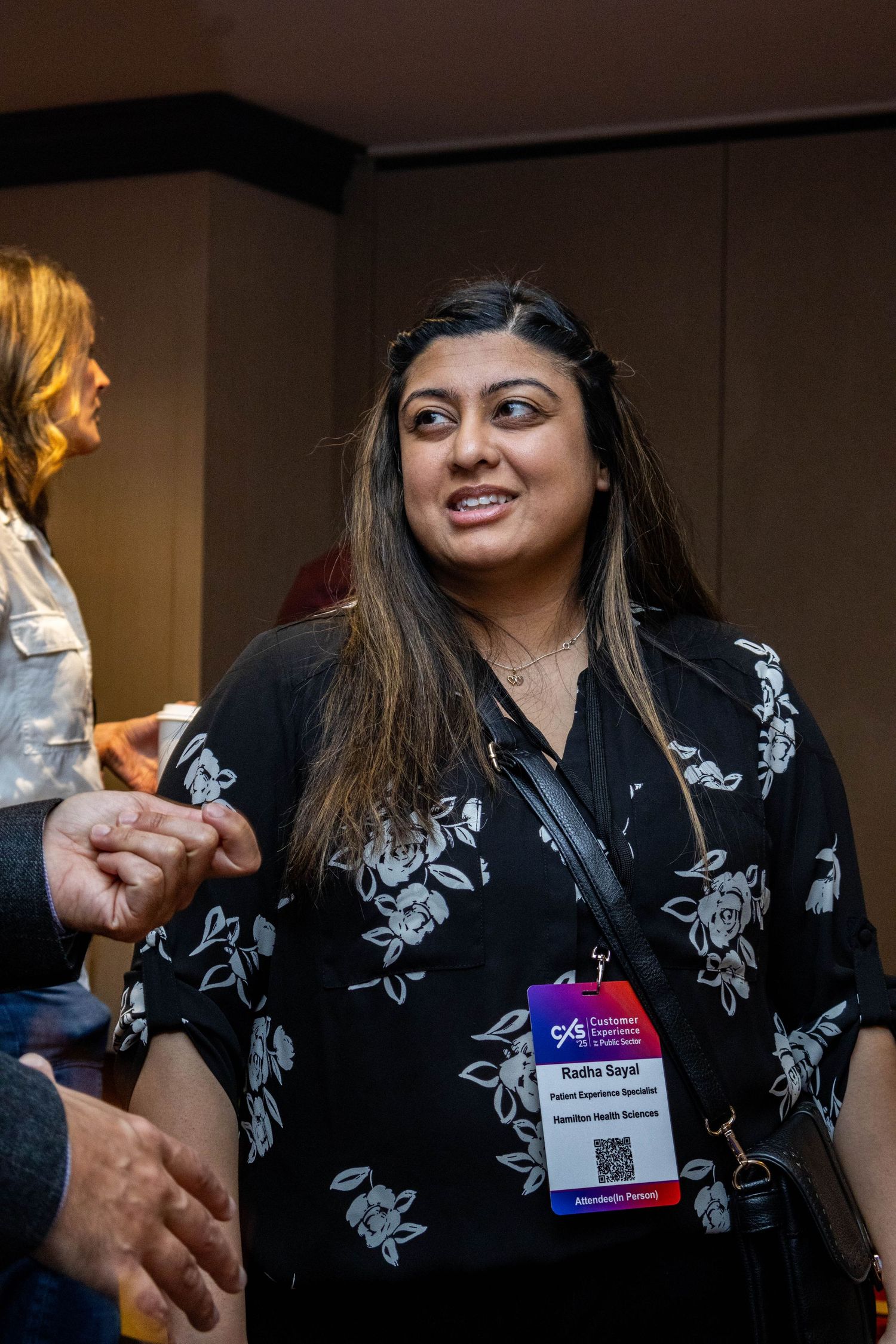 Conference attendee in floral print dress engages in conversation at professional networking event.