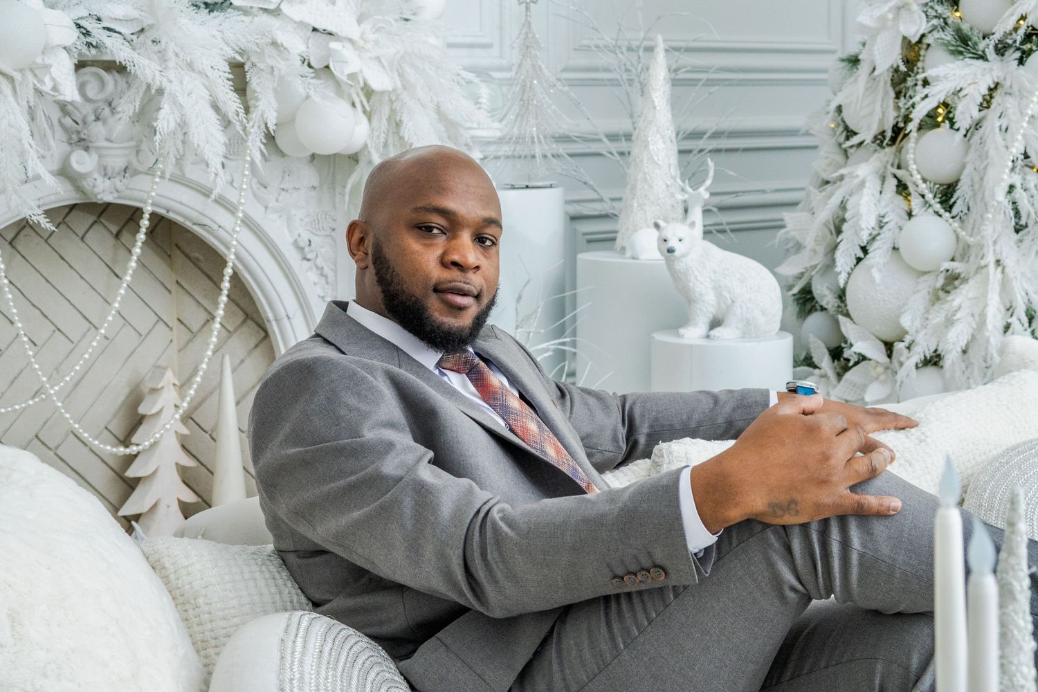 Professional in a gray suit sits comfortably on a white couch in an elegant white room with decorative elements.