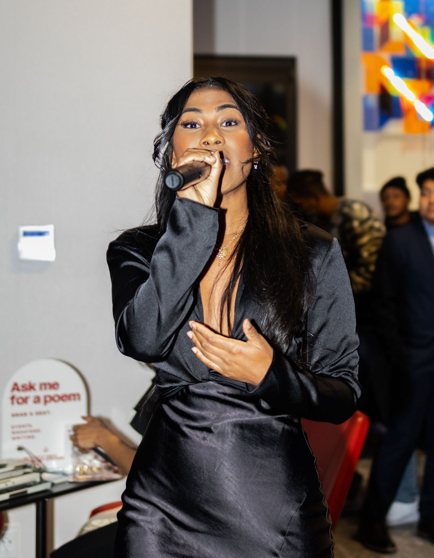 A performer in a black satin outfit sings emotively into a microphone at an indoor event.