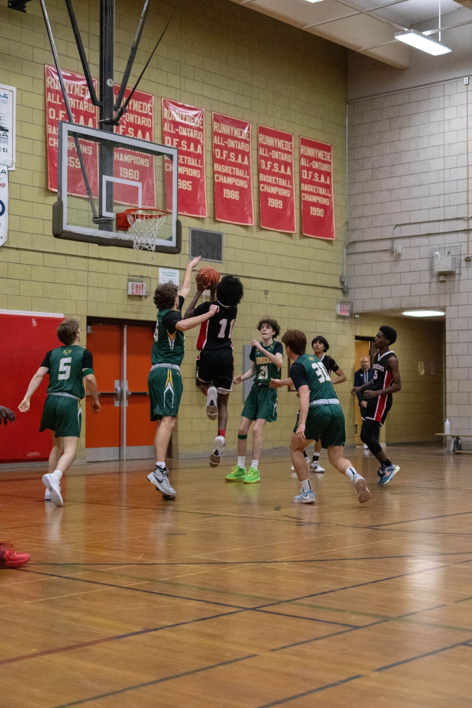 High school basketball players leap for a rebound during an intense indoor game on a wooden court.