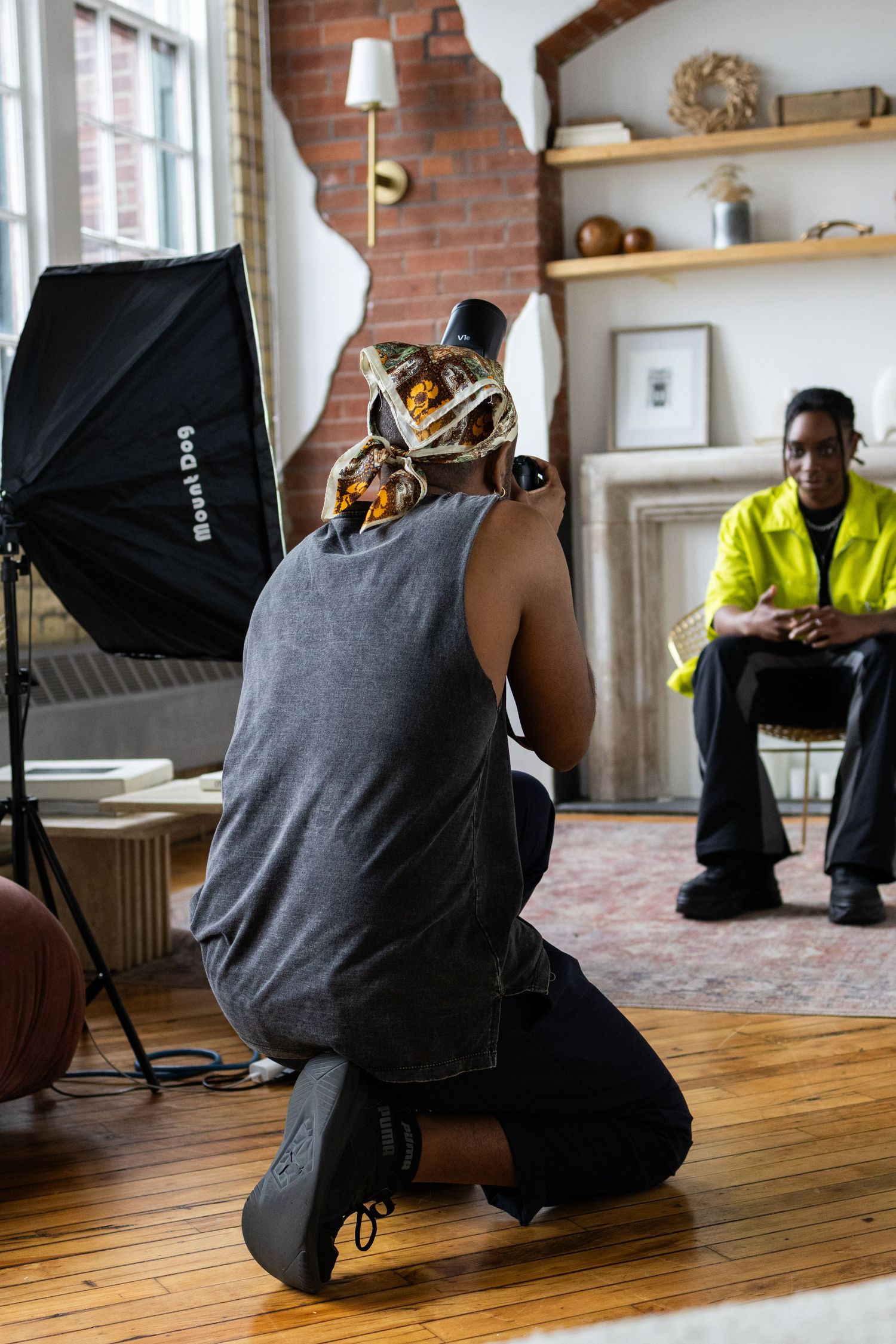 Photographer with camera kneeling to take photos in a studio setting with lighting equipment.