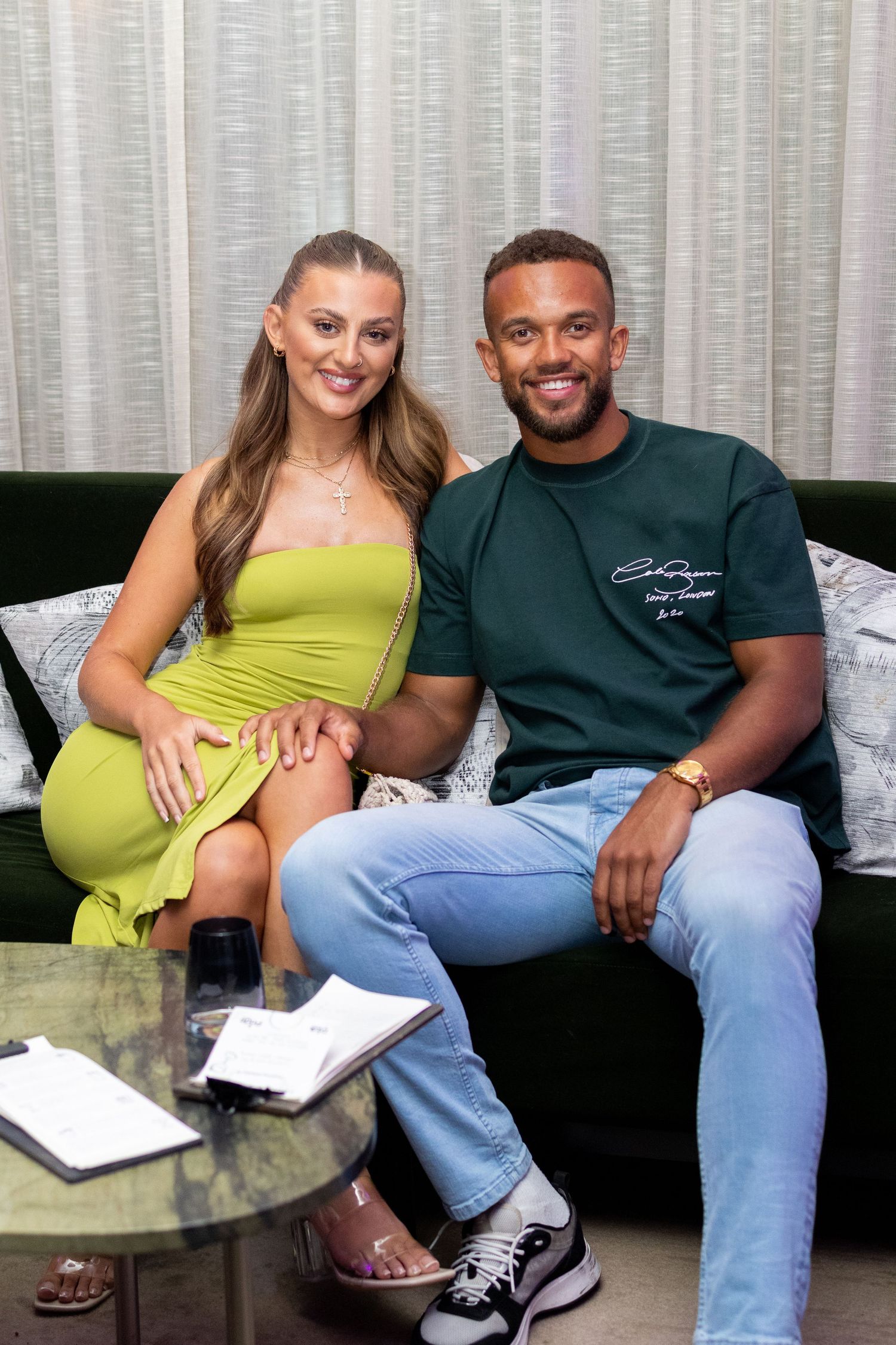 Couple relaxing on grey couch during casual photoshoot.