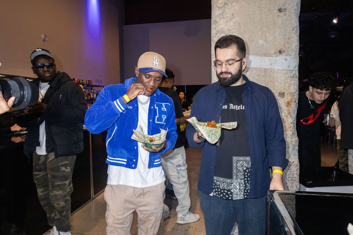 People enjoying food and drinks at a nighttime social gathering with blue lighting.